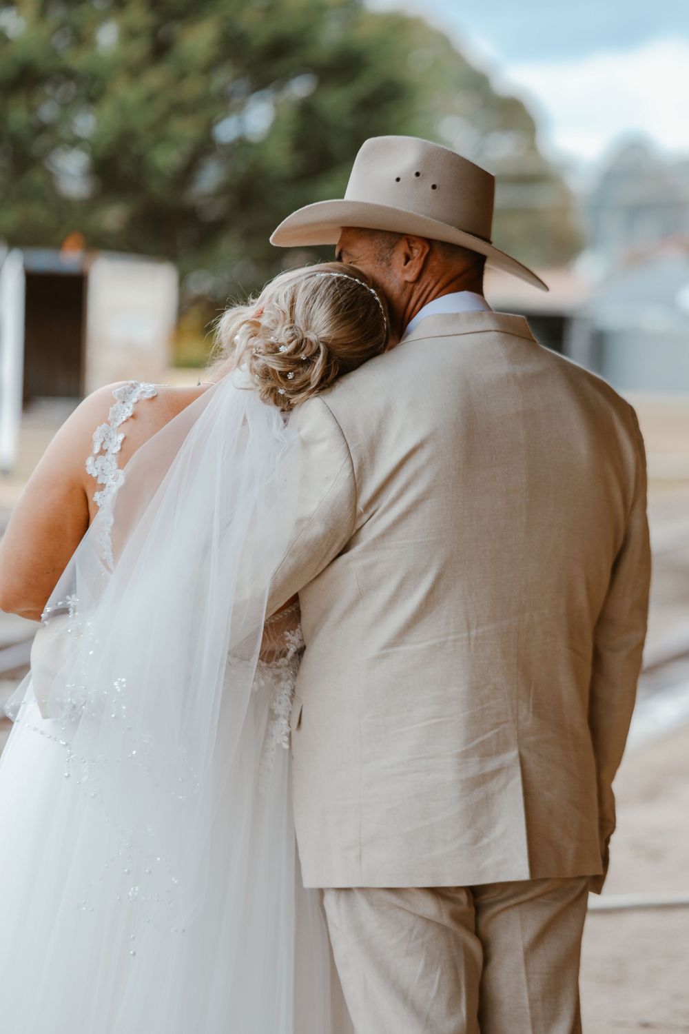 Close-up view of a bride in white dress and groom in beige suit from behind.