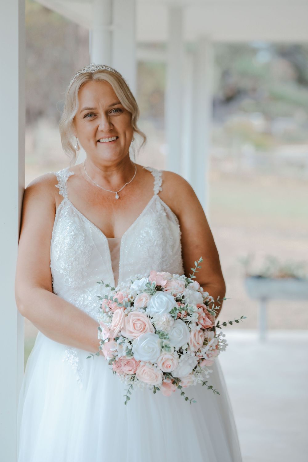 Bride in white lace wedding dress holds pink and white floral bouquet.