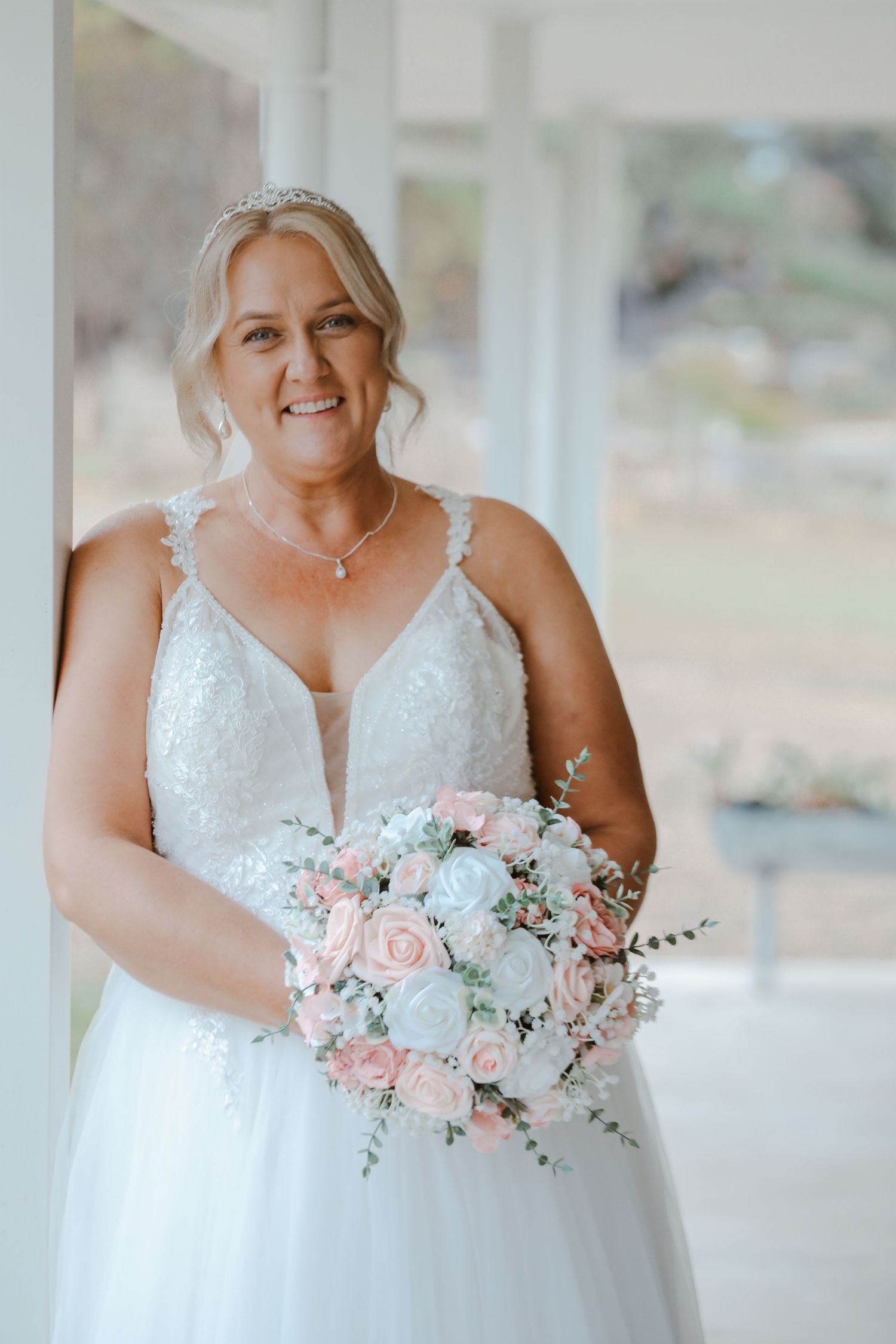Bride in white lace wedding dress holds pink and white floral bouquet.