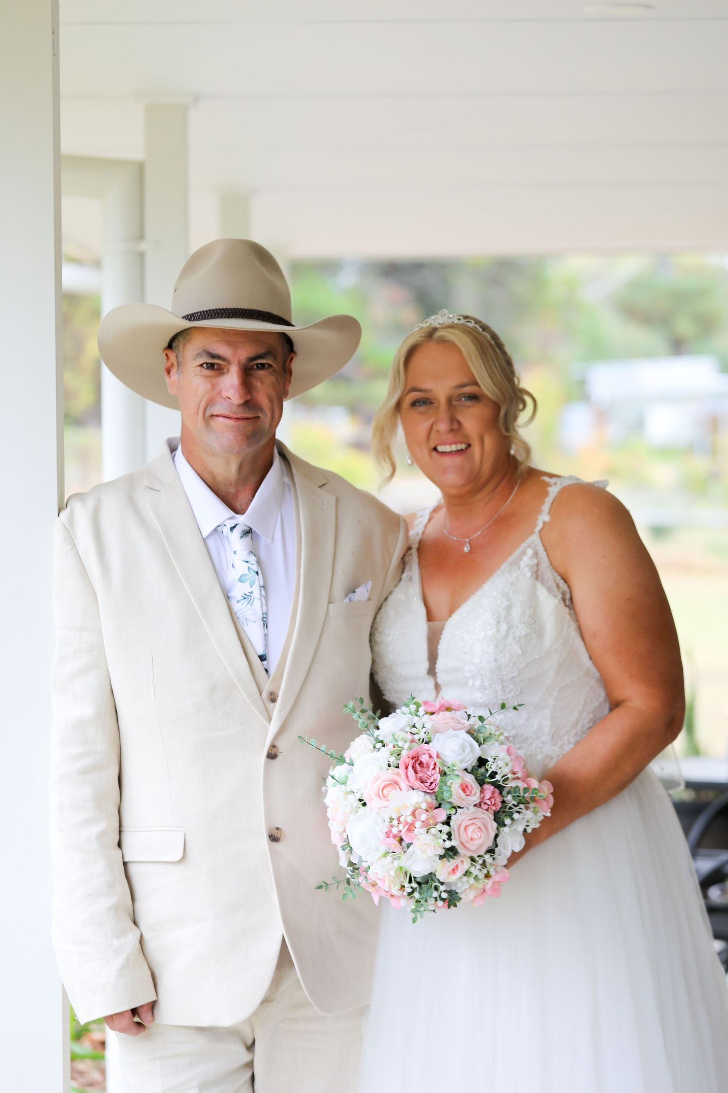 Western-themed wedding couple poses together under white columns with pink floral bouquet.