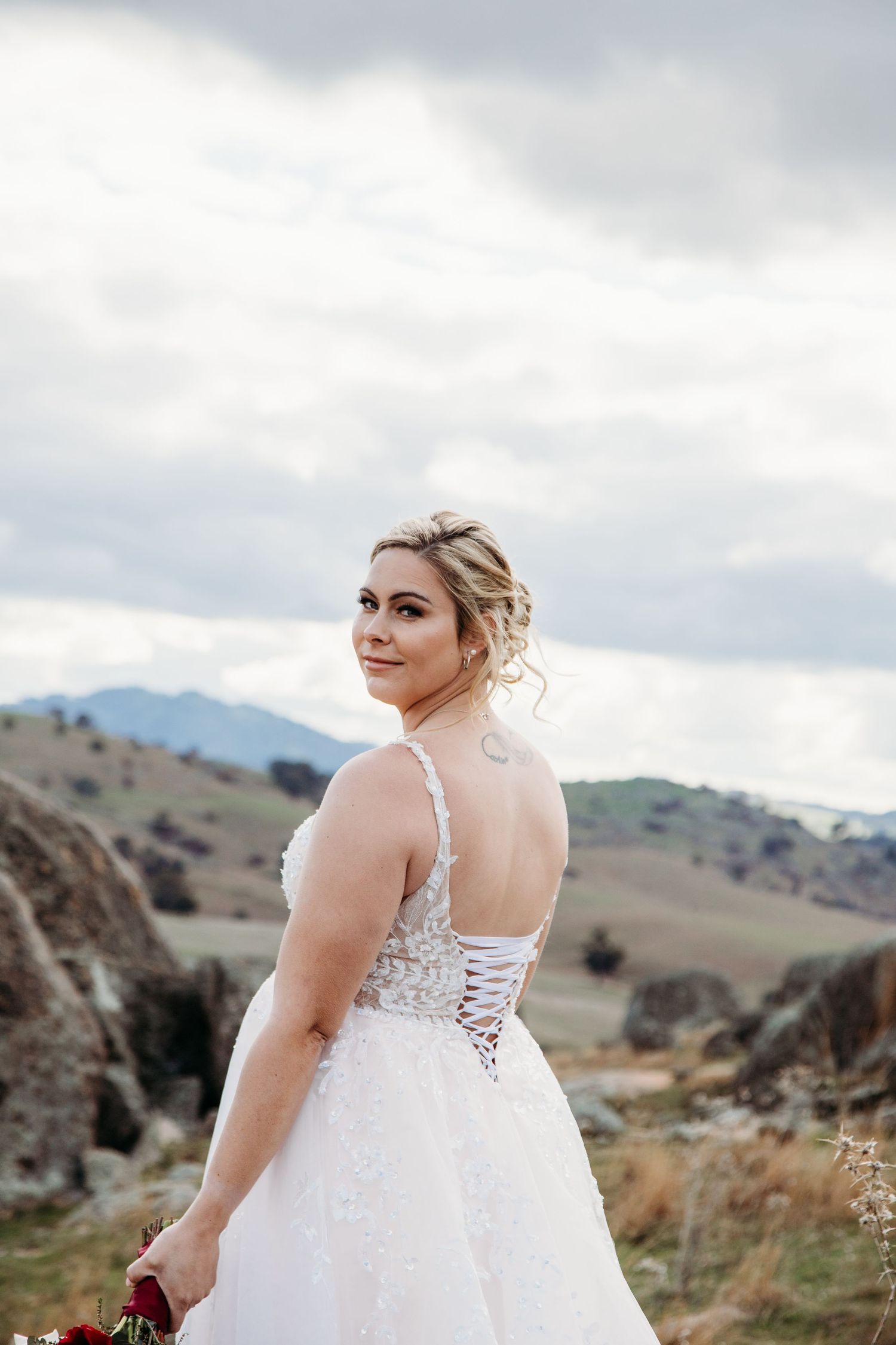 A white lace wedding dress with corset back detail shown against mountainous landscape.