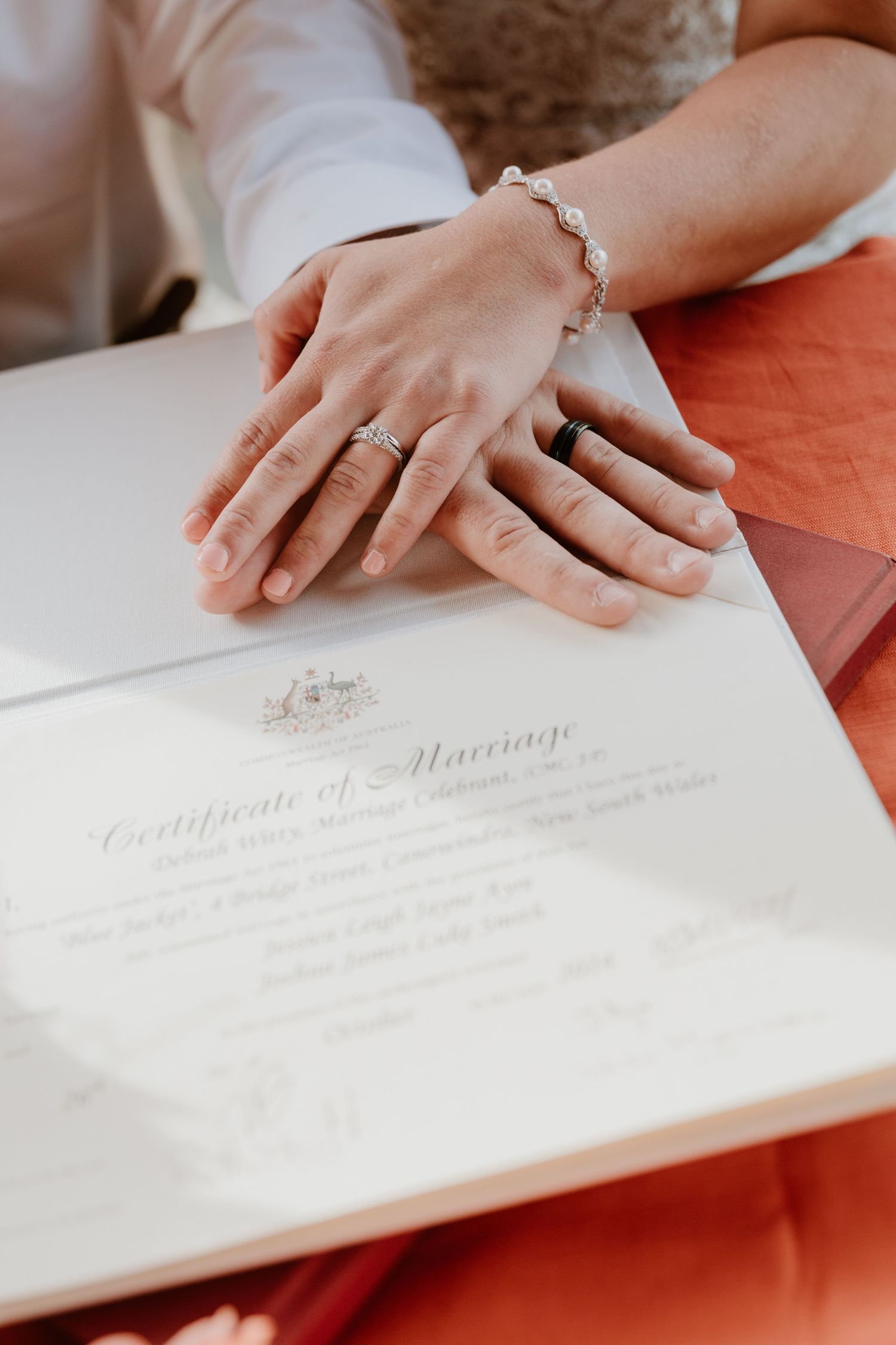 Marriage certificate being signed with close-up views of hands and rings against a white document.