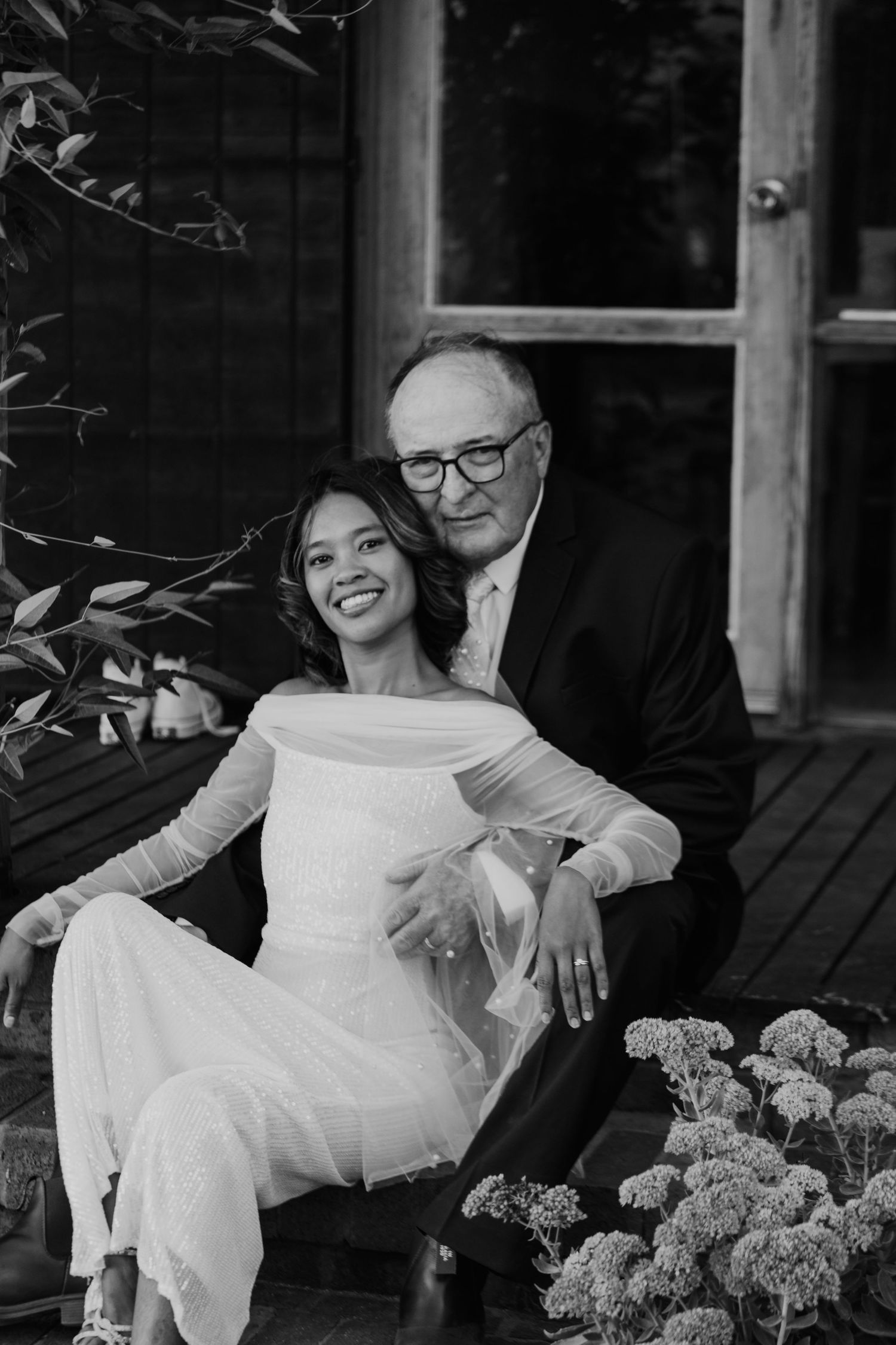 A couple relaxes on a porch with white hydrangea flowers in an intimate black and white portrait.