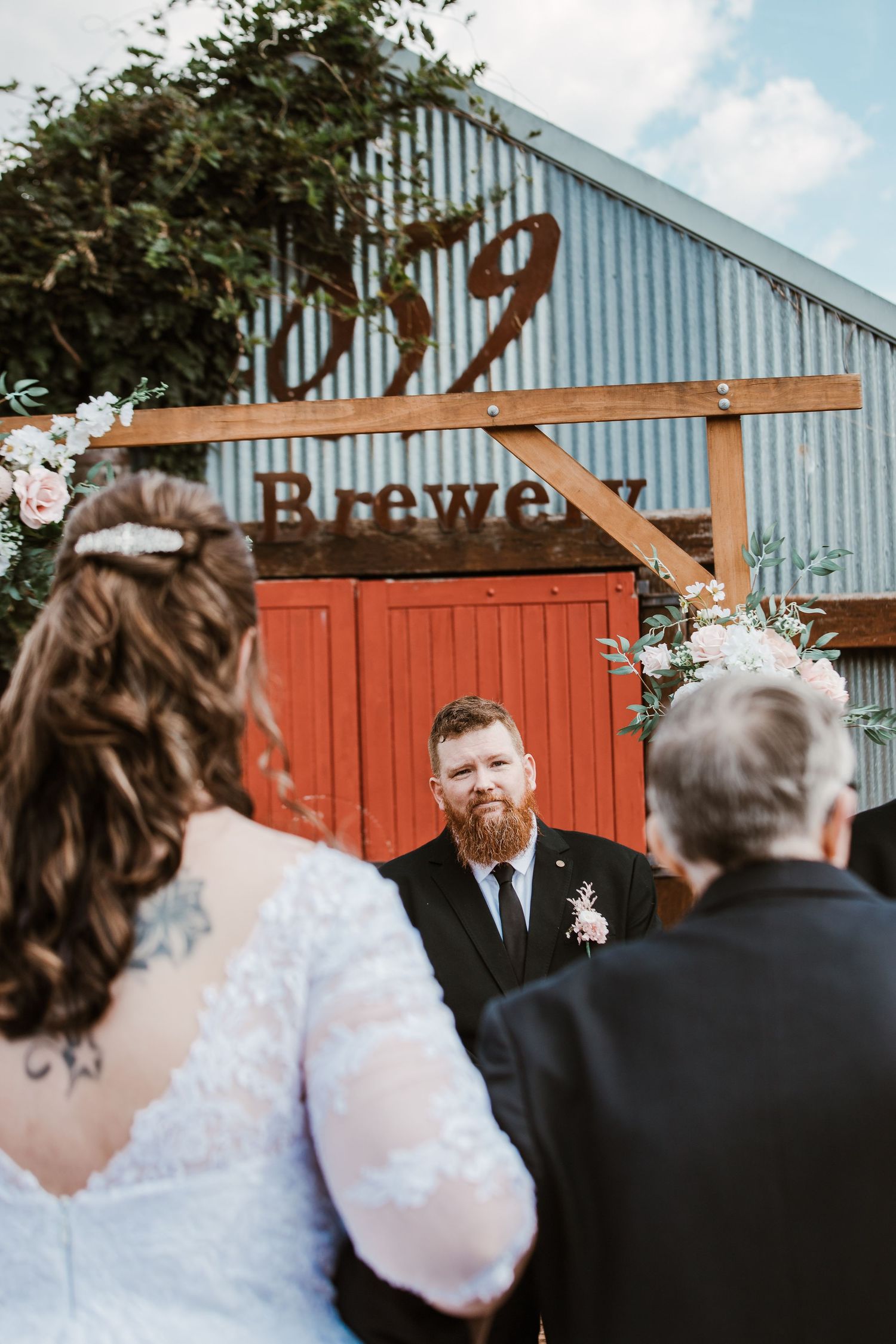 Outdoor wedding ceremony scene with rustic barn and red fence backdrop.