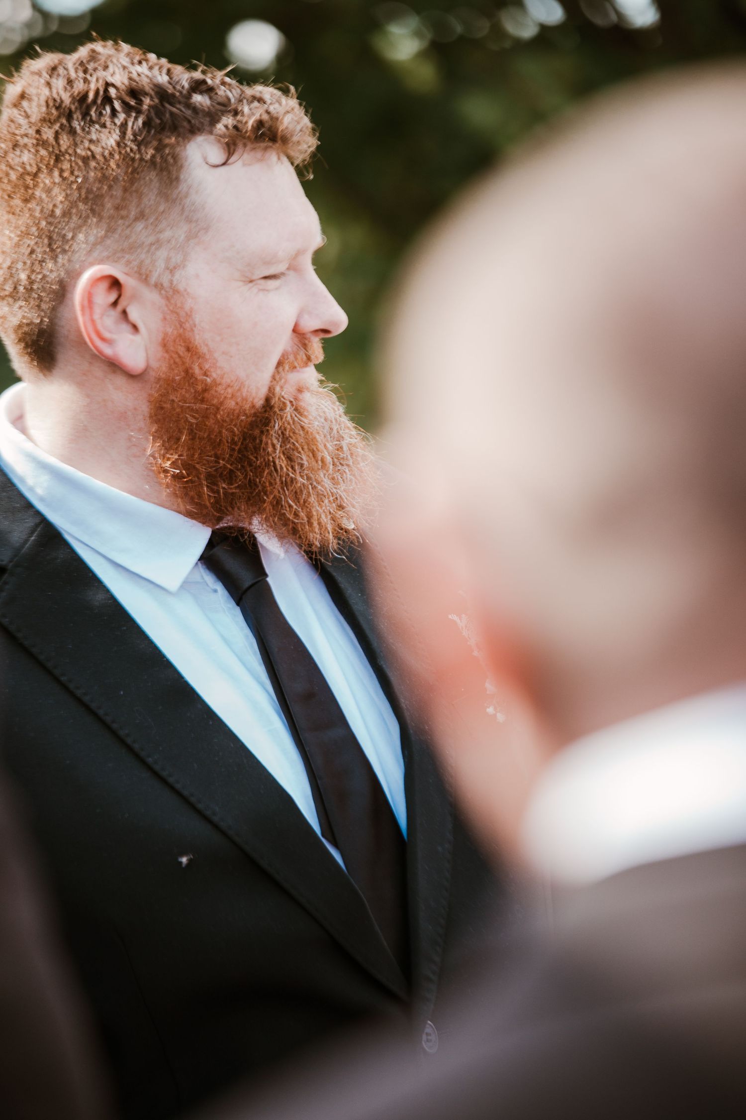 Close-up profile shots of a groom with red beard wearing formal black suit and tie.