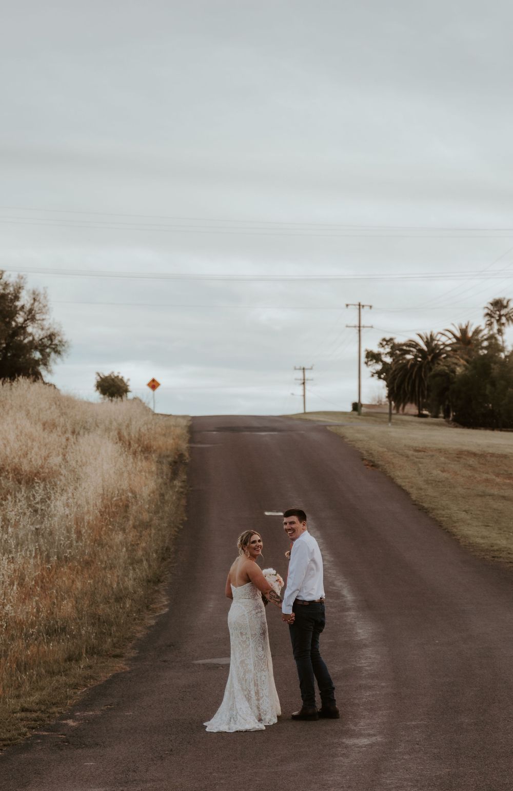Couple in formal attire sharing an intimate moment on a rural dirt road at sunset.