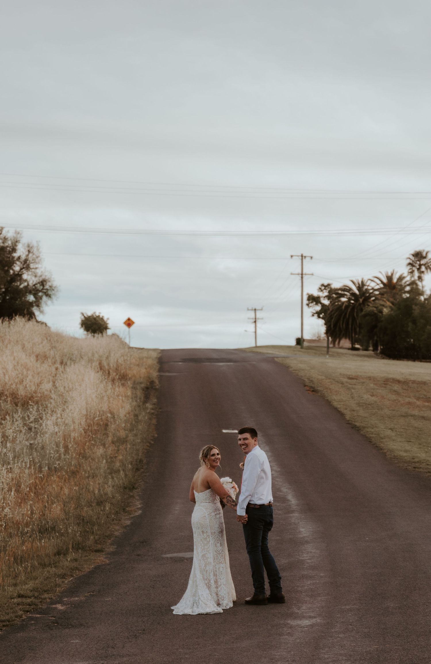 Couple in formal attire sharing an intimate moment on a rural dirt road at sunset.