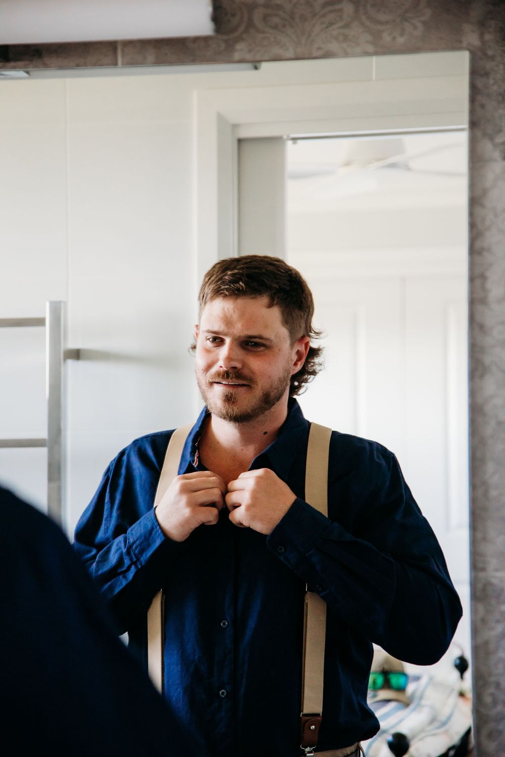 Person wearing navy blue shirt and suspenders adjusts collar in preparation.