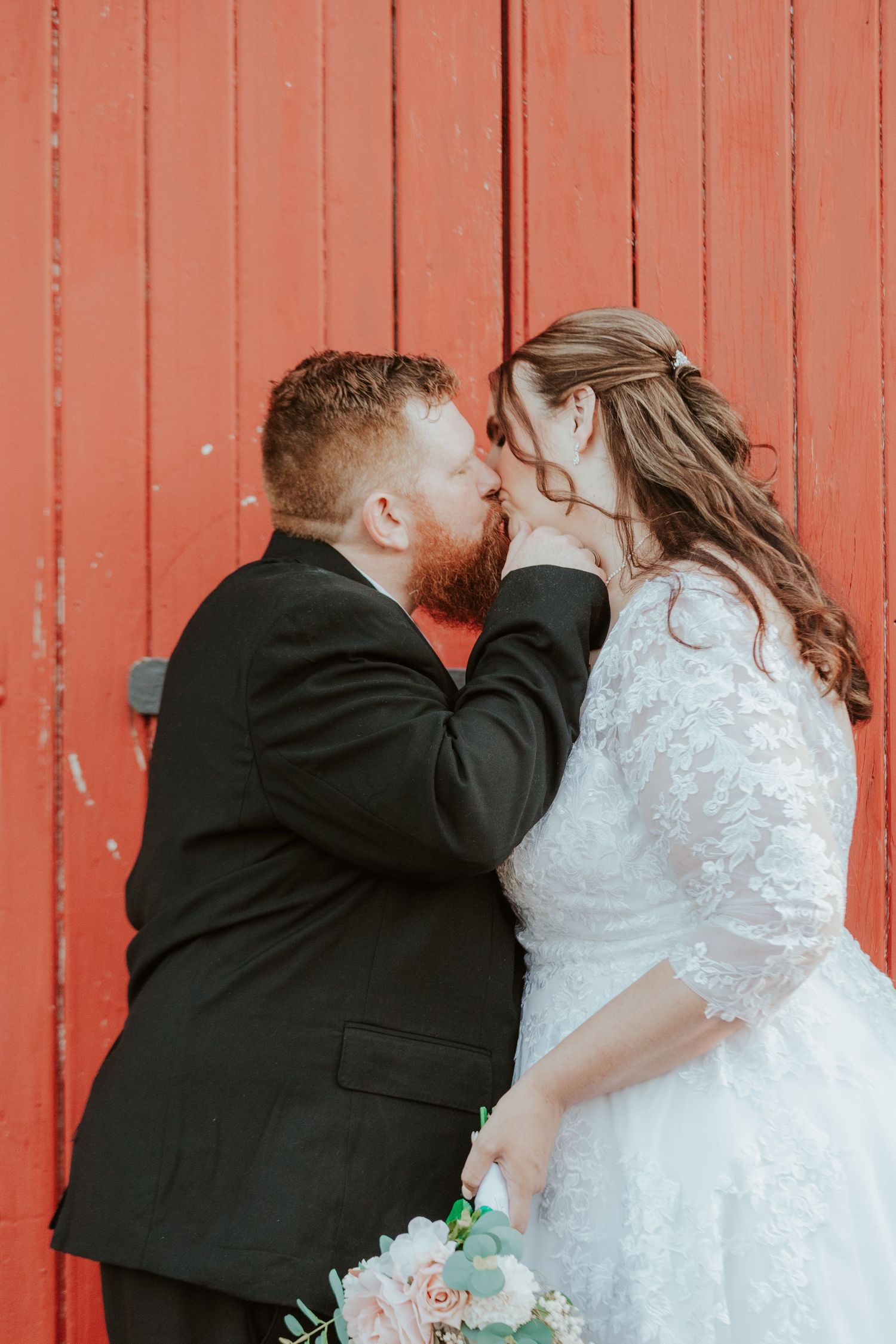Series of wedding portraits against a red barn wall showing tender moments between the couple.