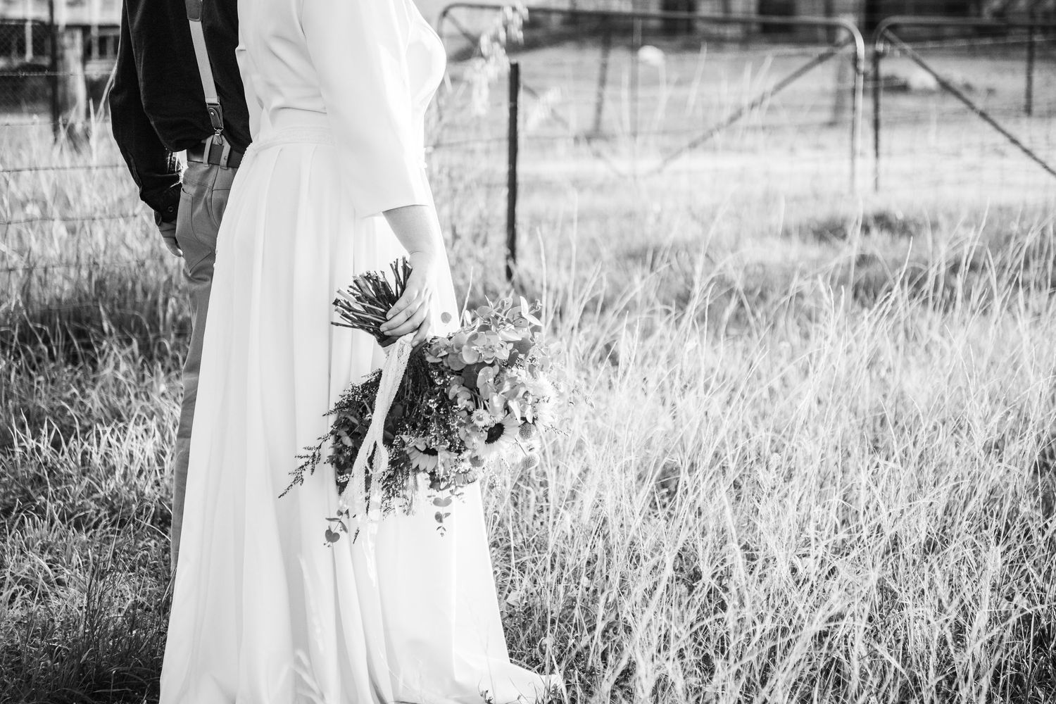 Black and white intimate wedding portraits taken in a grassy field with dramatic lighting and rustic elements.