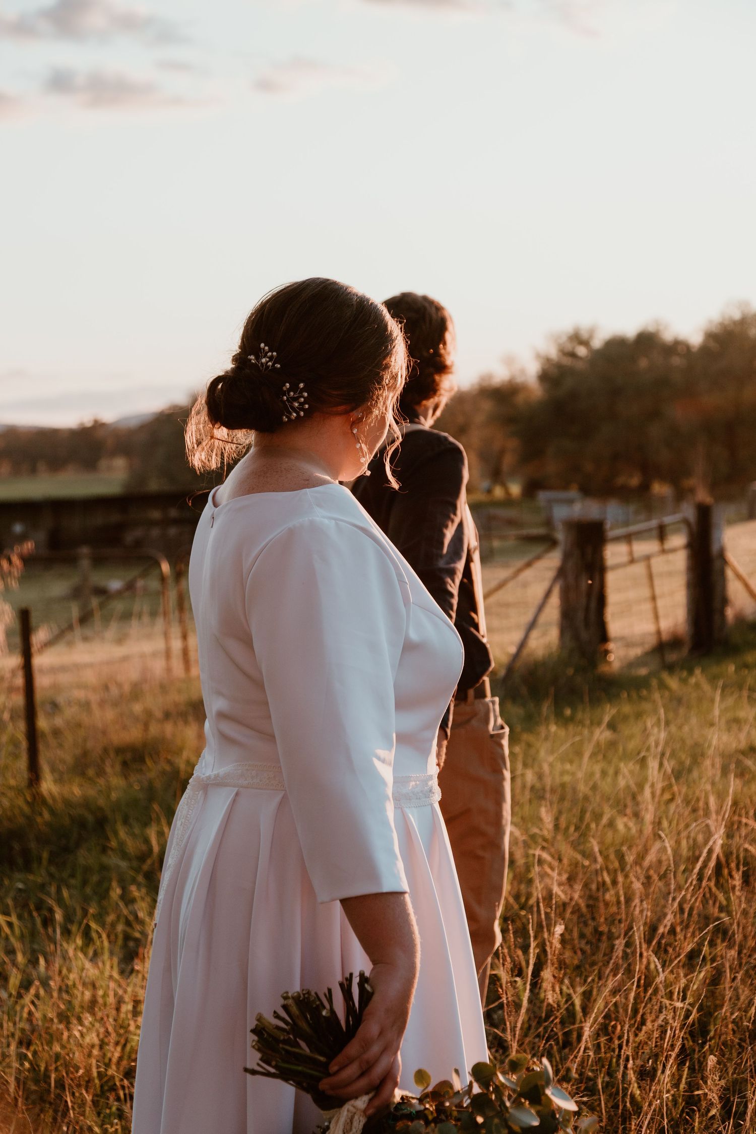 Wedding couple embracing in golden sunlit field with tall grass at sunset.