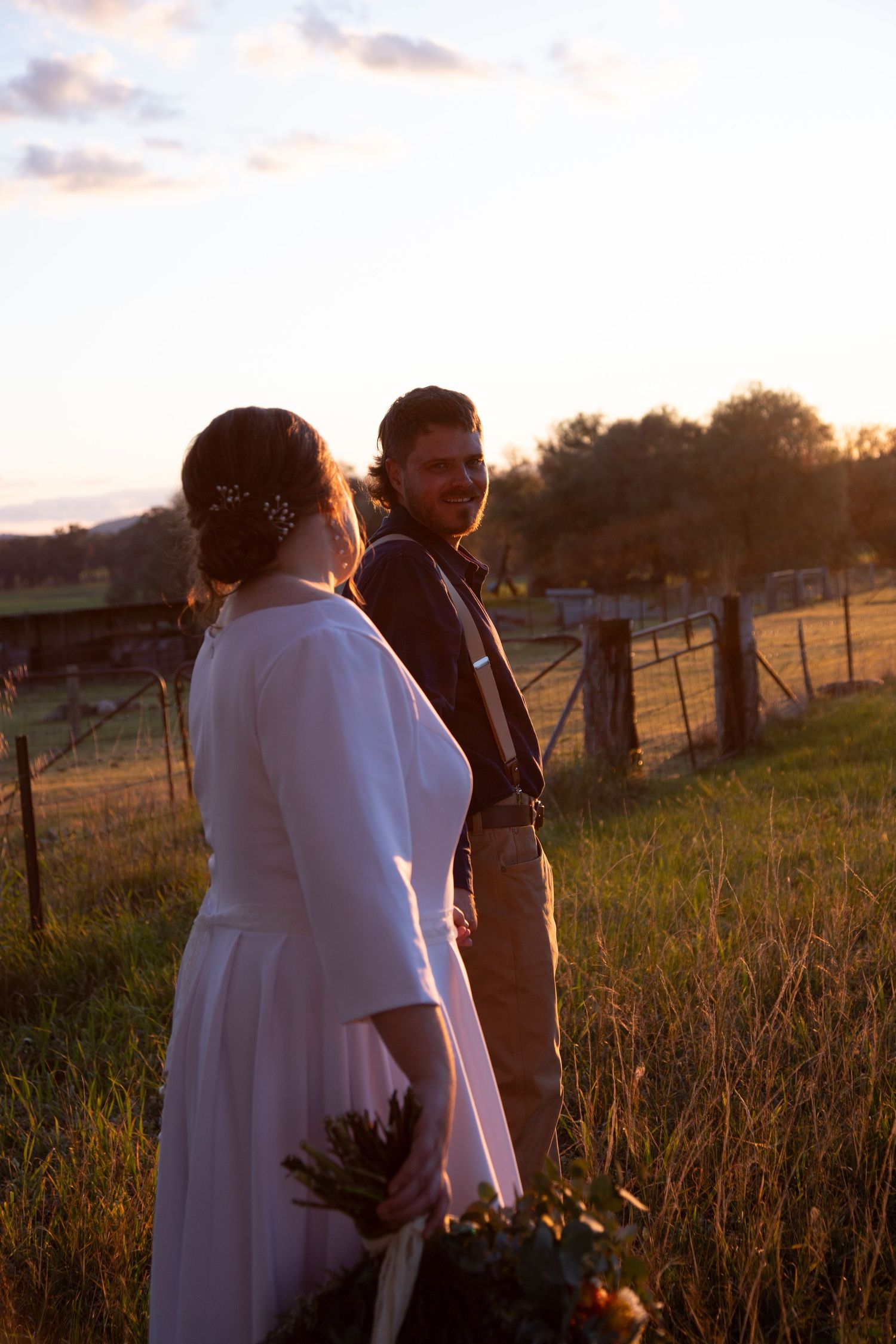 Wedding couple walking through a golden sunset field with warm backlighting and rural countryside views.