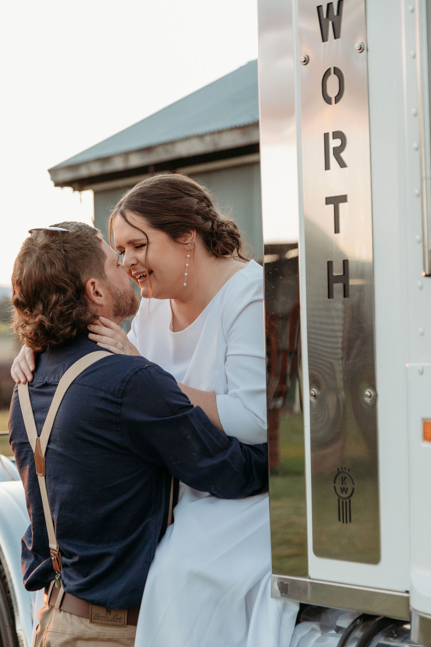 Couple shares intimate moment against rustic white building wall outdoors.