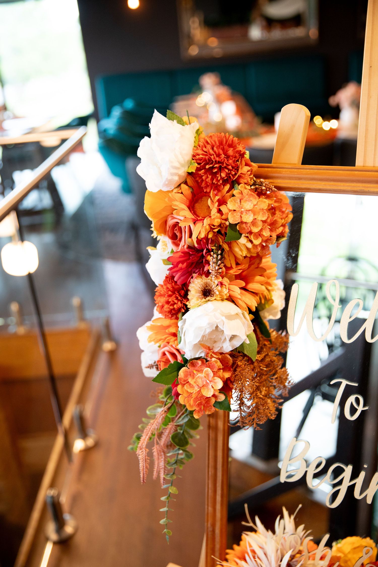 Autumn-themed wedding decor featuring orange and peach floral arrangements with signage.