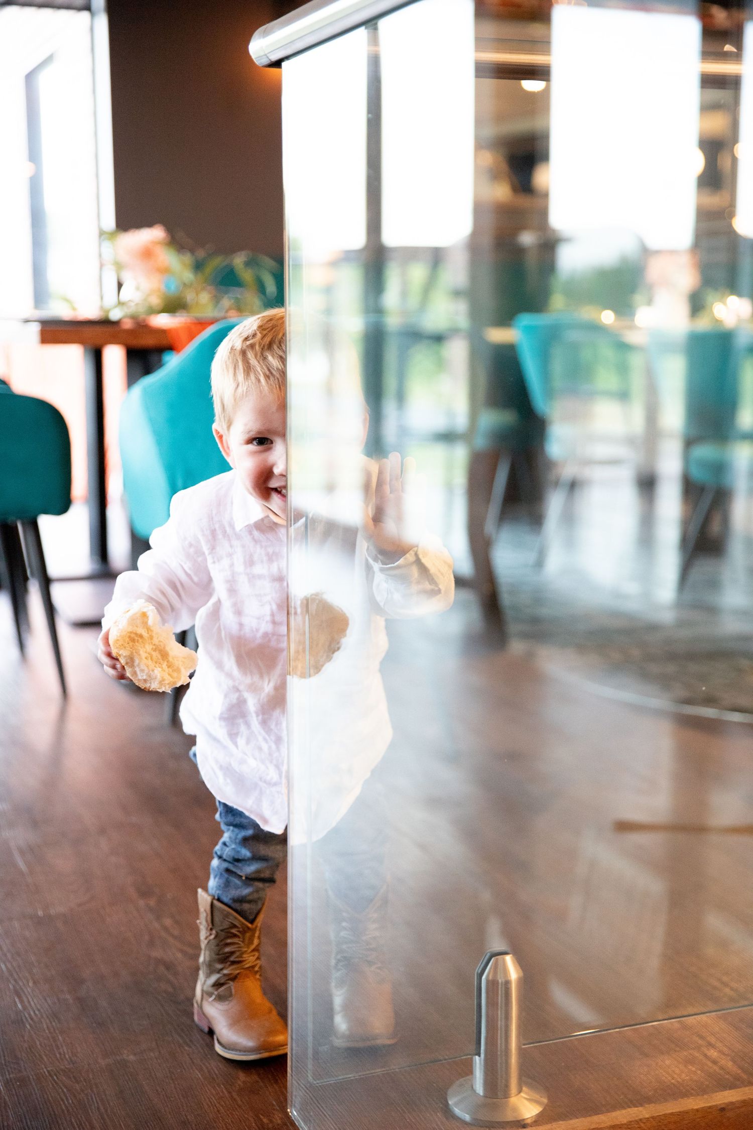 Small child in white shirt playing on hardwood floor near glass windows.