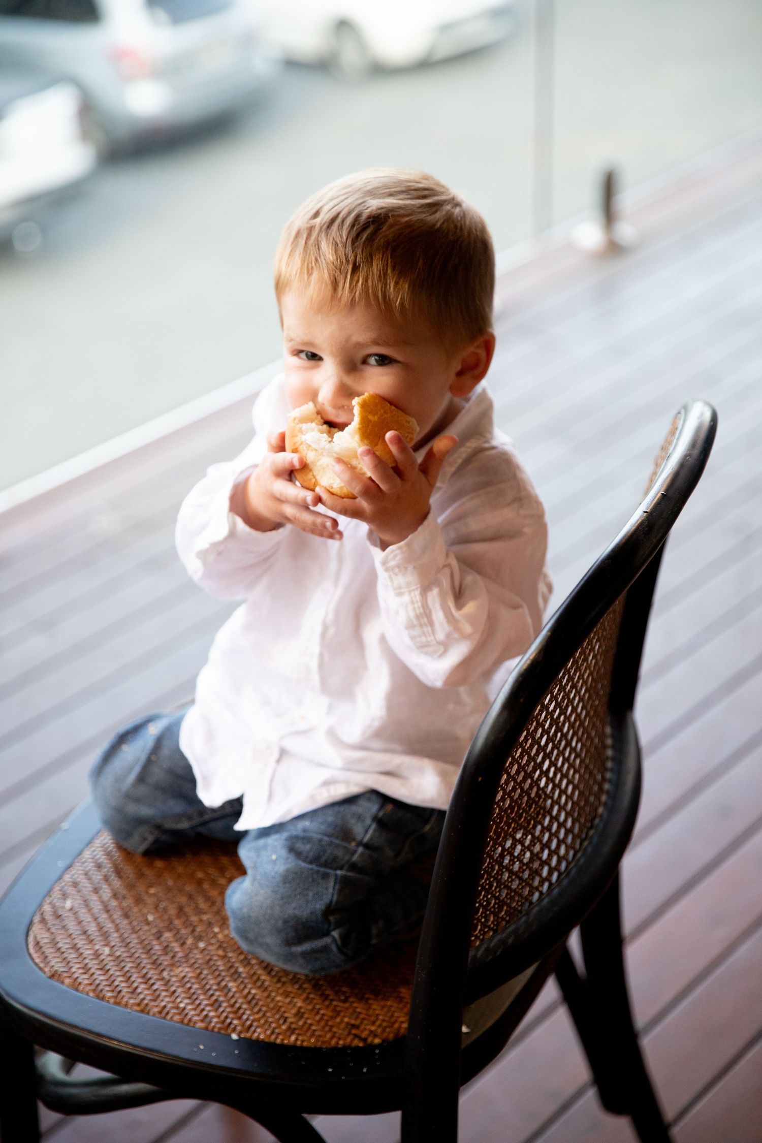 Young child eating snack while sitting in dark wicker chair.