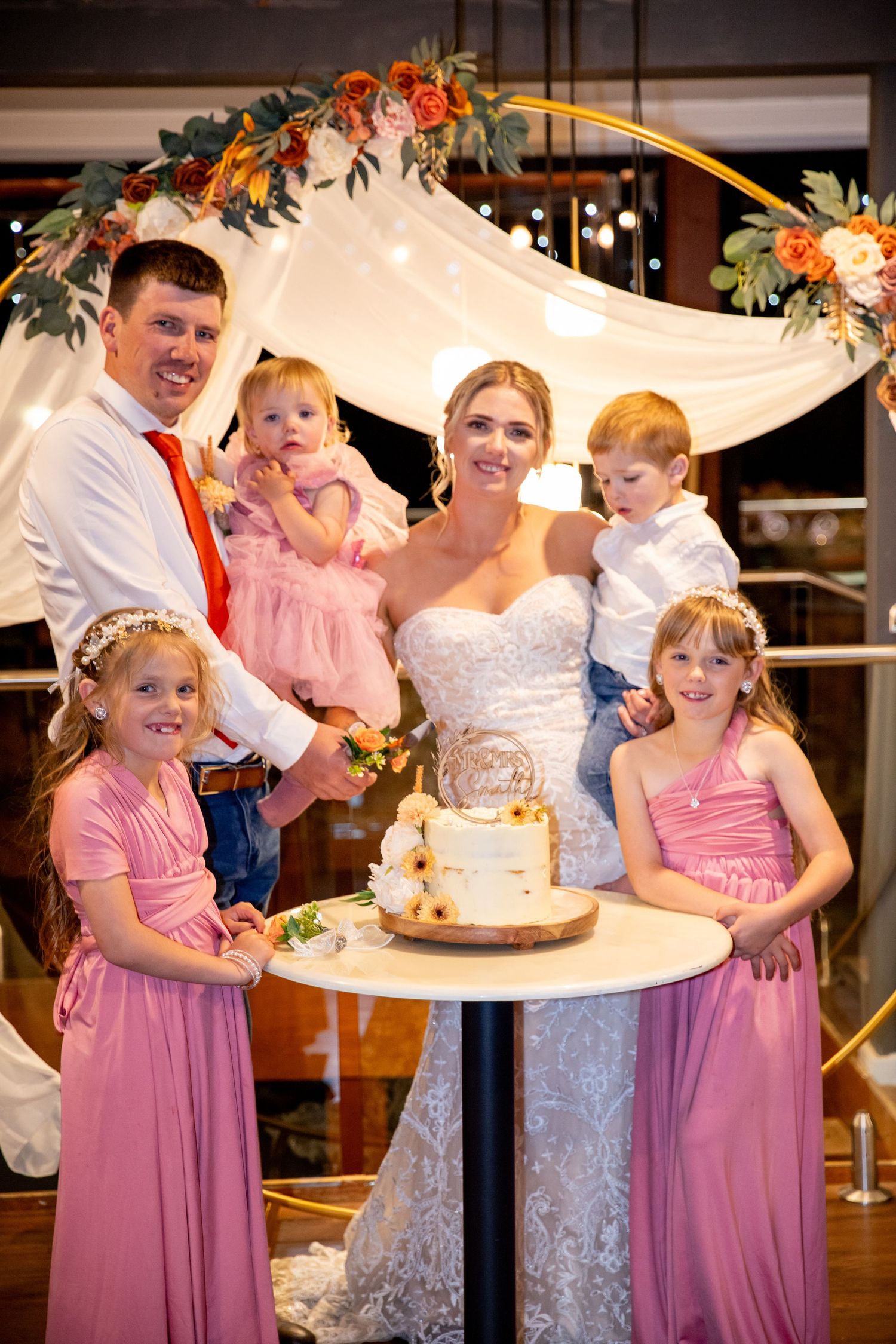 Wedding party celebrating around a cake cutting with pink and white decor.