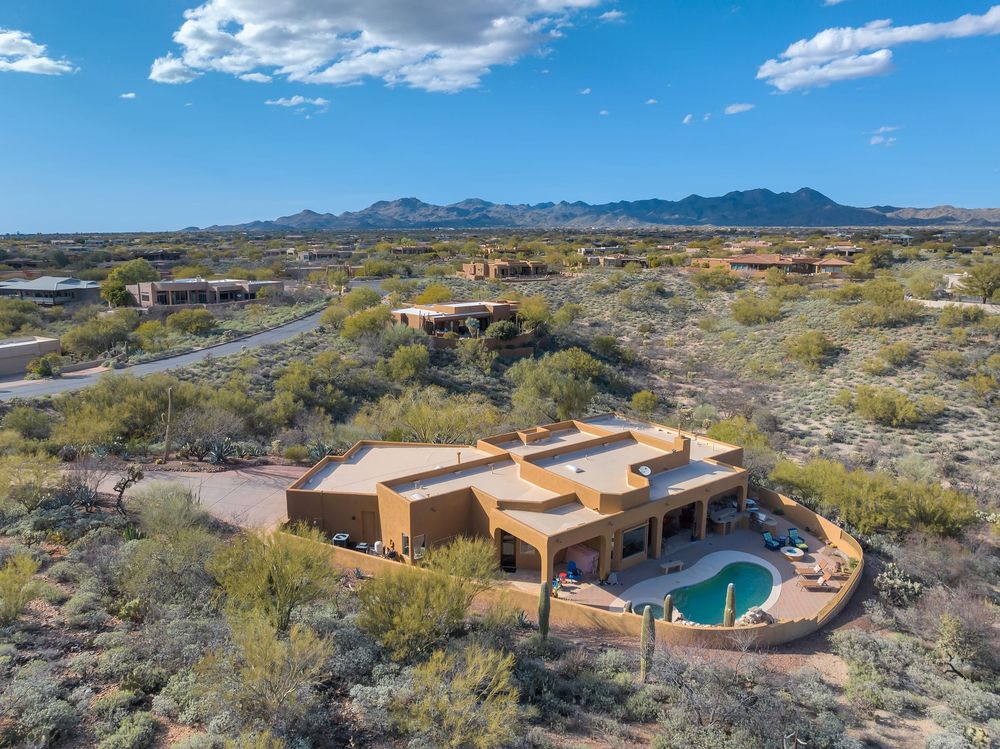 Aerial panoramic view of a modern desert home with swimming pool surrounded by rugged Sonoran Desert landscape and mountains.