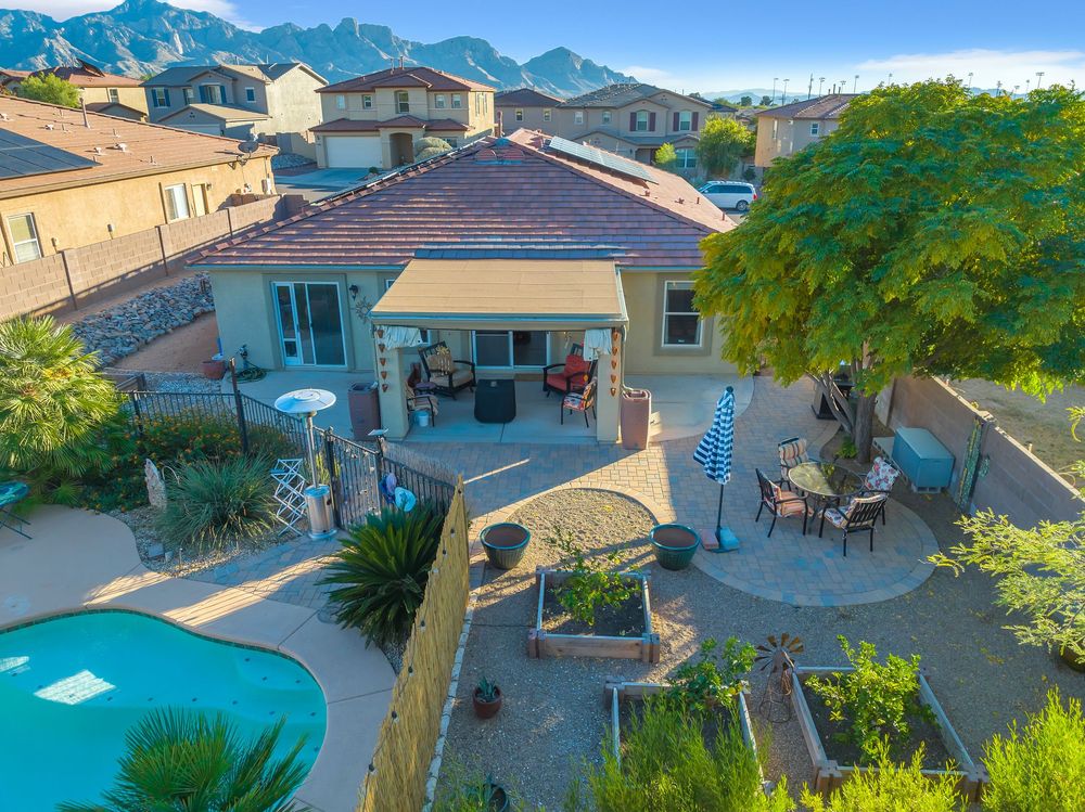 Aerial view of a luxurious backyard with swimming pool, covered patio, and mountain landscape in the background.