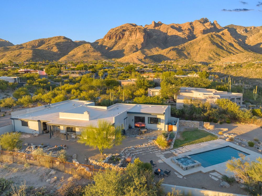 Panoramic view of luxury desert homes nestled against rugged mountains with a swimming pool at sunset.