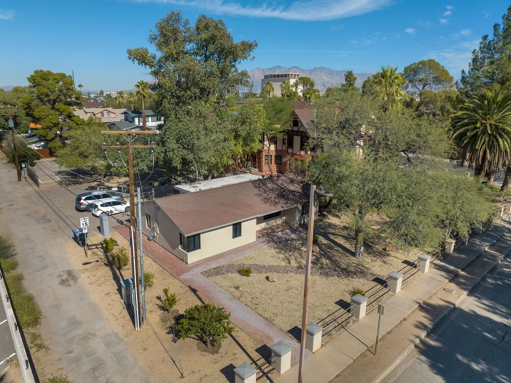 Aerial view of a small church building with brown roof surrounded by trees and parked cars on a sunny day.