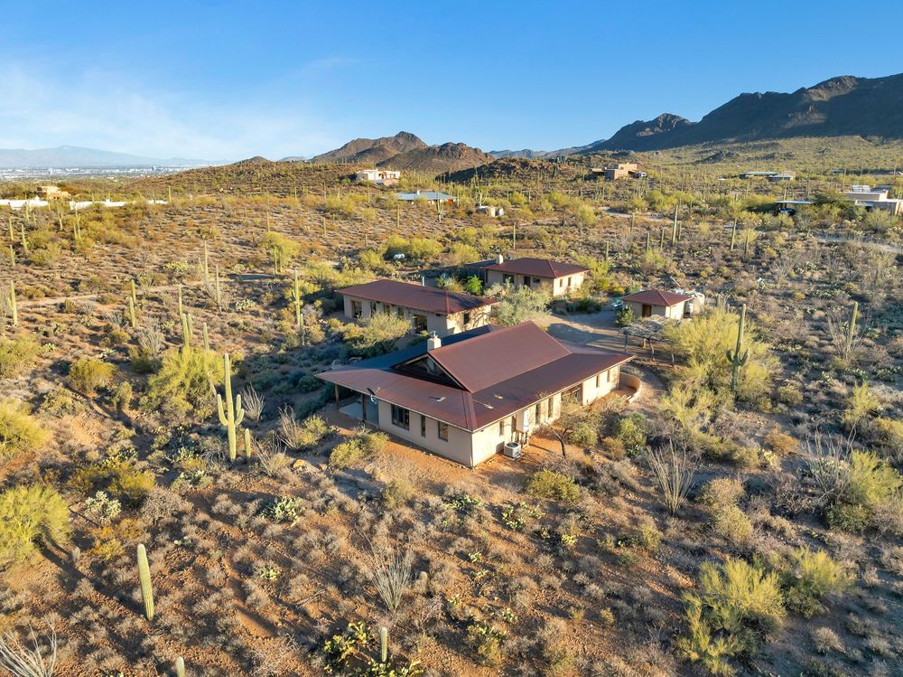 Panoramic desert landscape with scattered ranch-style homes nestled among rocky terrain and native vegetation at sunset.