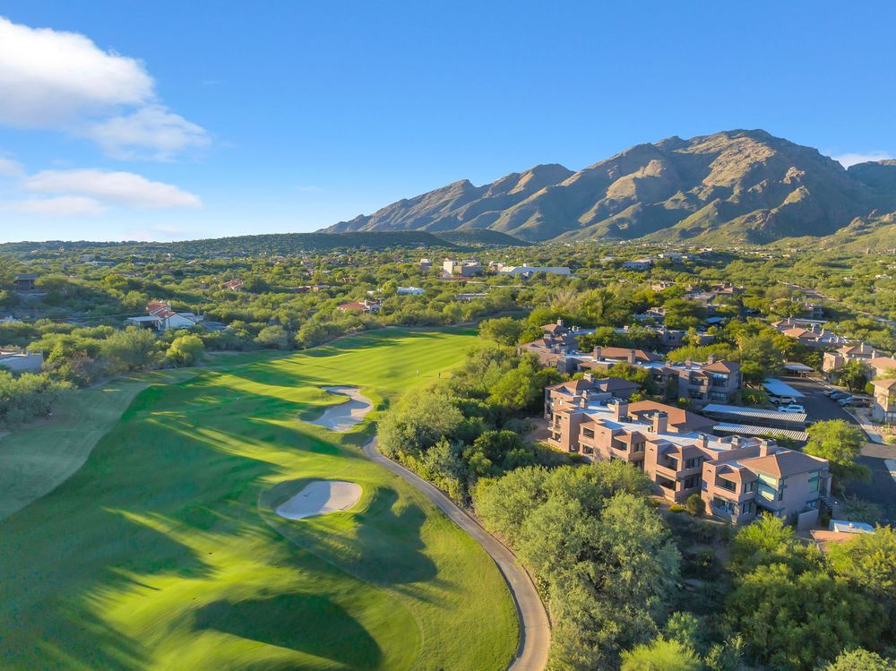 Panoramic aerial view of a golf course nestled in mountains with lush green fairways and residential buildings nearby.