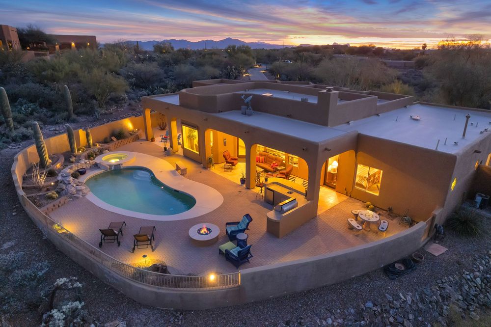 Aerial views of a luxurious desert home with curved pool and outdoor living spaces illuminated at sunset.