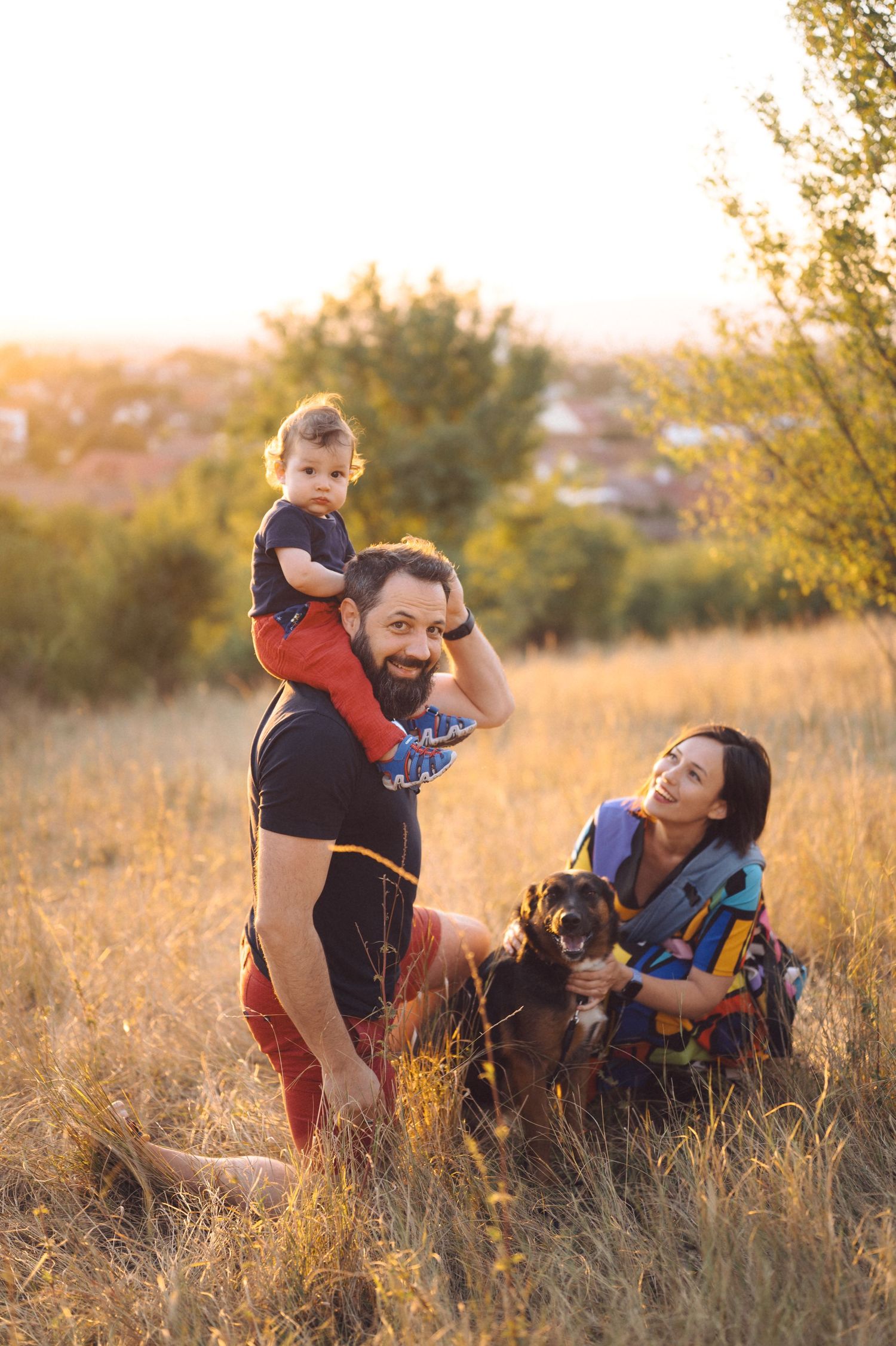 Family enjoying a warm autumn sunset together in golden grass field with a small dog.