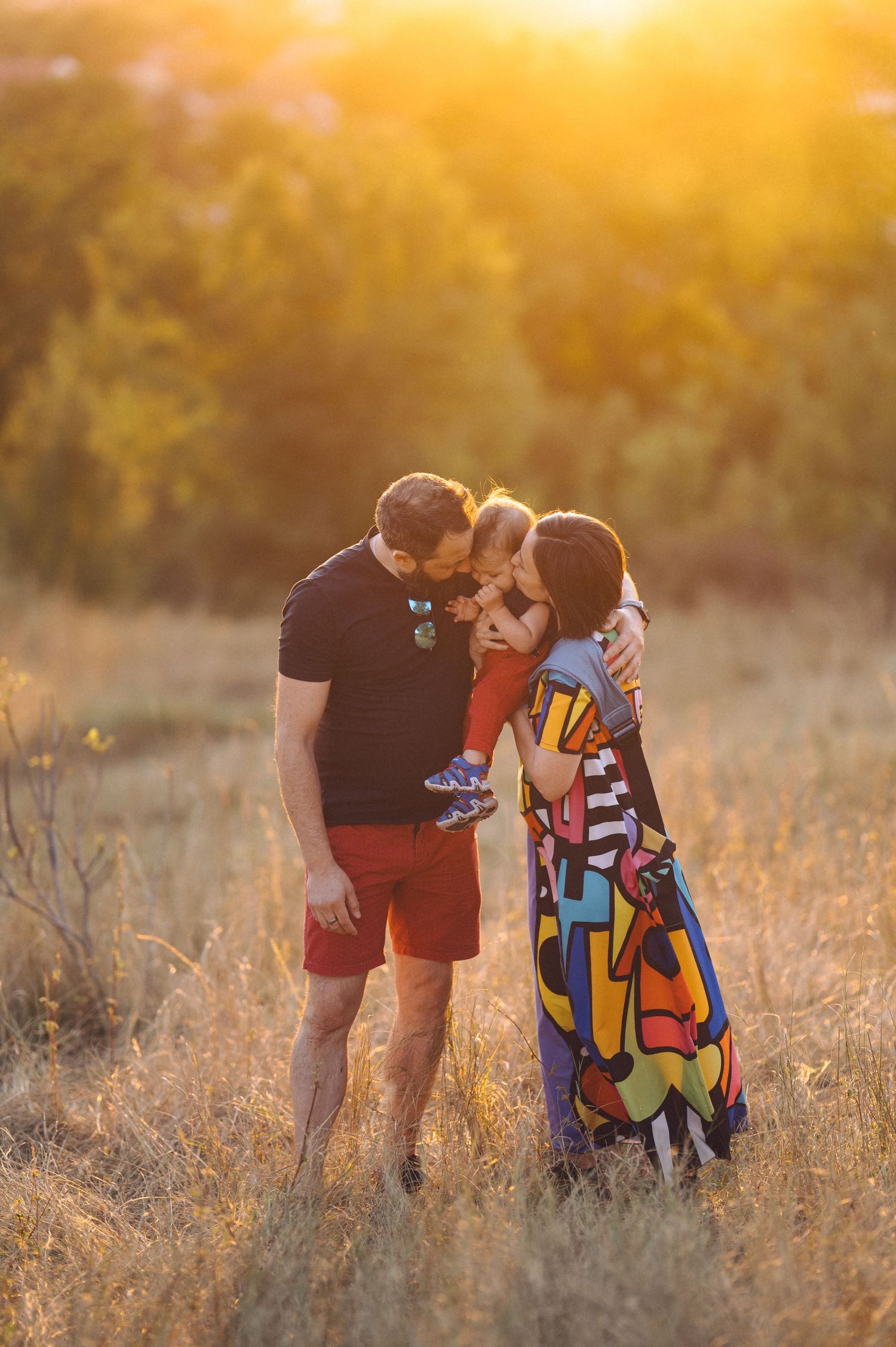 Family having tender moments in a golden wheat field at sunset with beautiful backlit lighting.