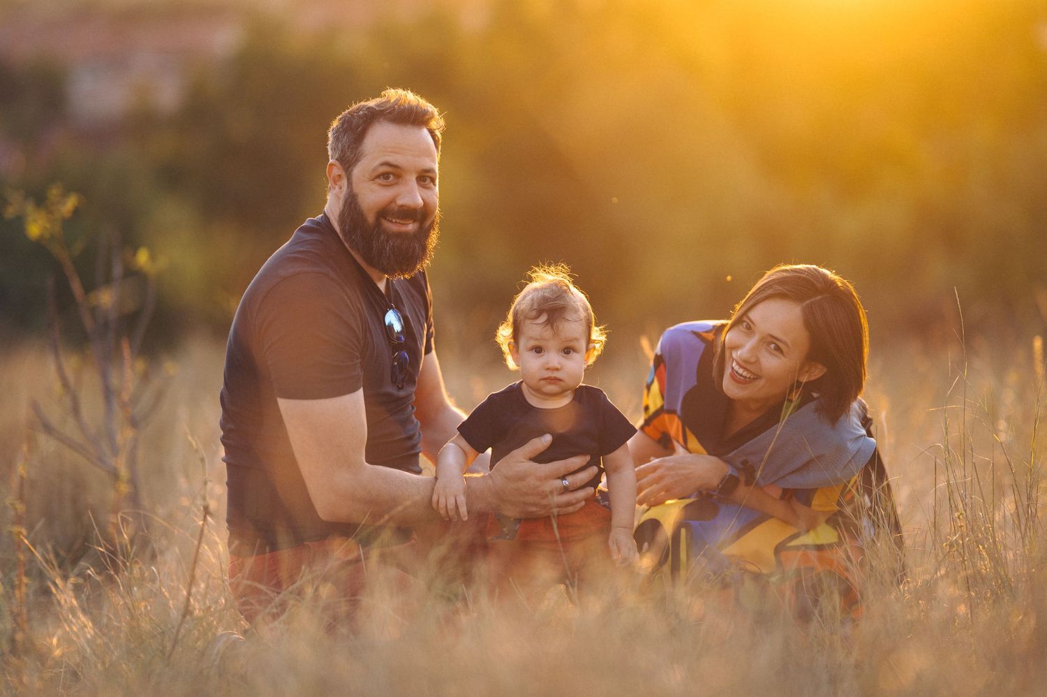 Happy family enjoying picnic in golden field at sunset as they sit together and share food outdoors.