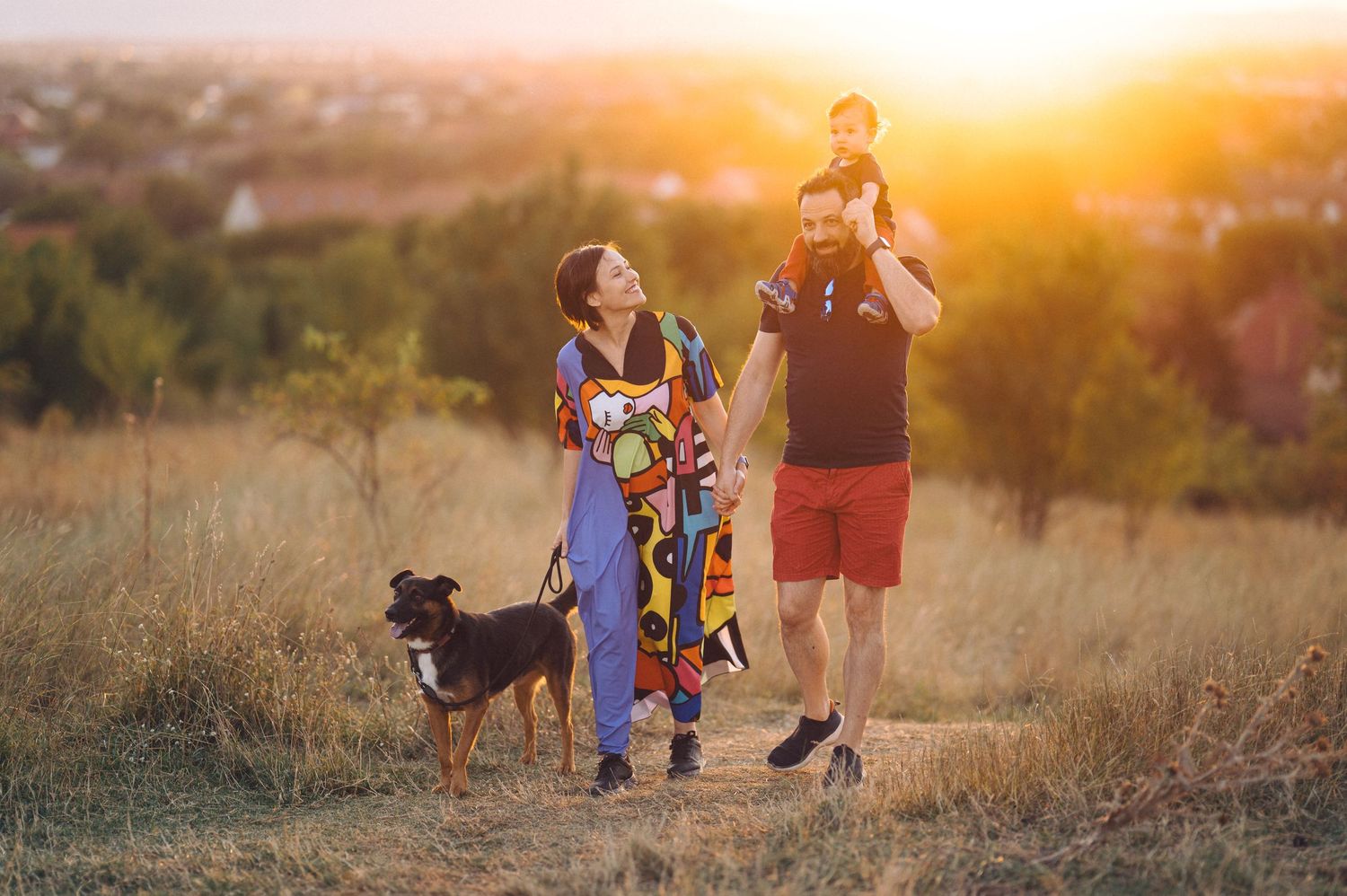 A family and their dog standing in a golden field at sunset while spending time together outdoors.