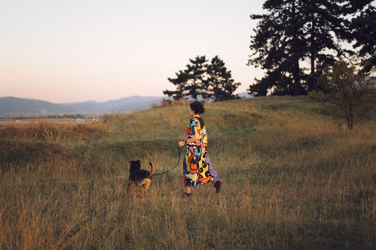 An electric bike and two people traverse a scenic grassy hillside during sunset with long shadows casting across meadow.