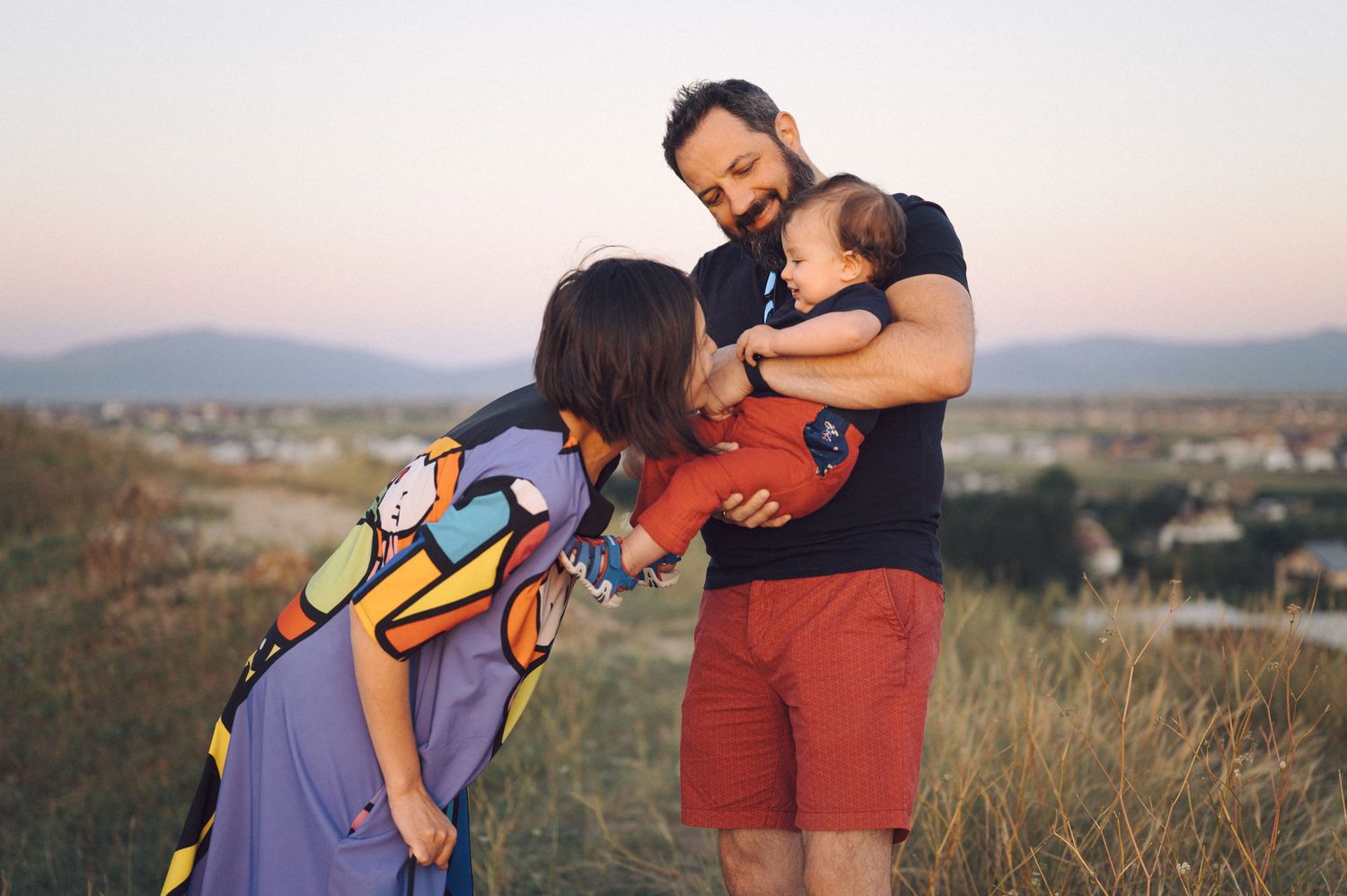 People enjoying sunset views from a hilltop meadow with soft golden lighting and distant landscape scenery.