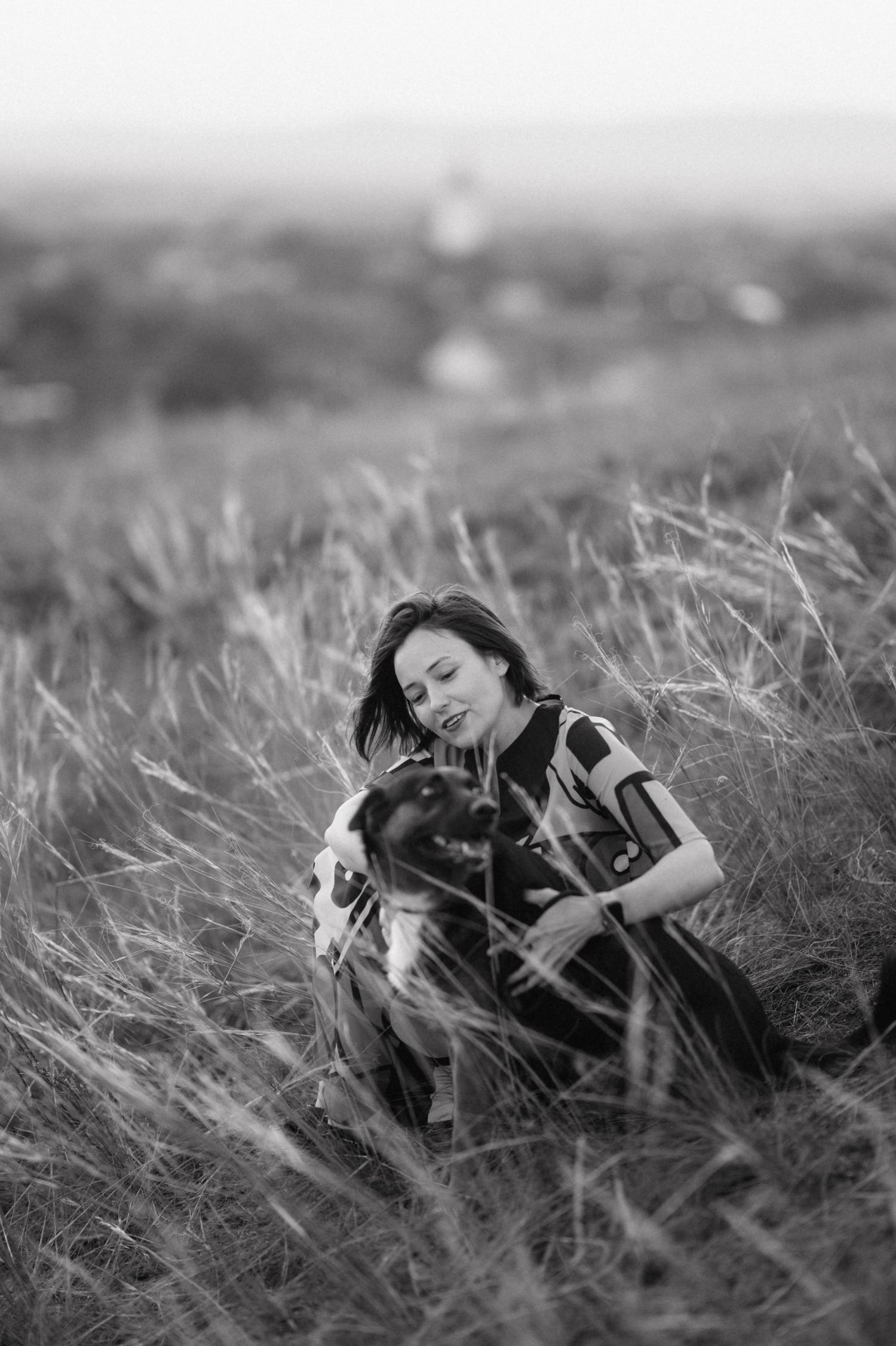 A person lies peacefully in tall grass wearing black clothing in a black and white artistic photograph.