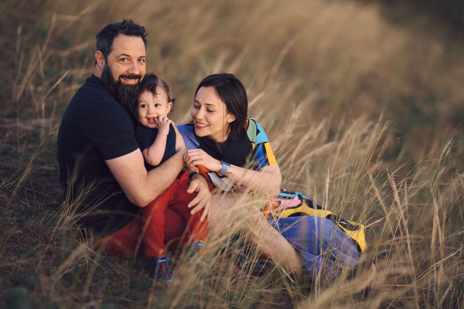 Family laying in tall grass during outdoor lifestyle photo session in warm afternoon sunlight.