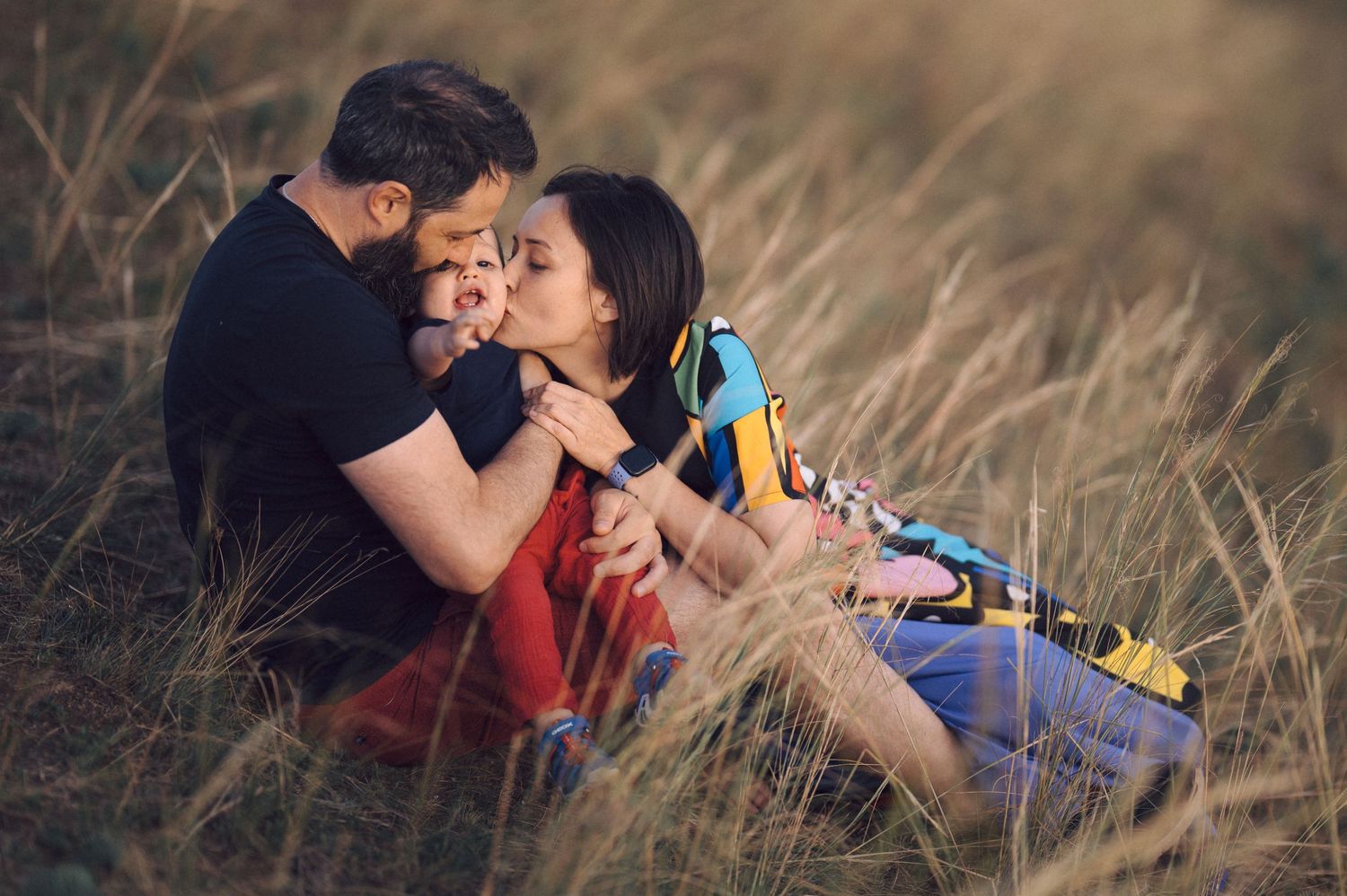 Couple embraces tenderly in tall grass field during golden hour photoshoot.