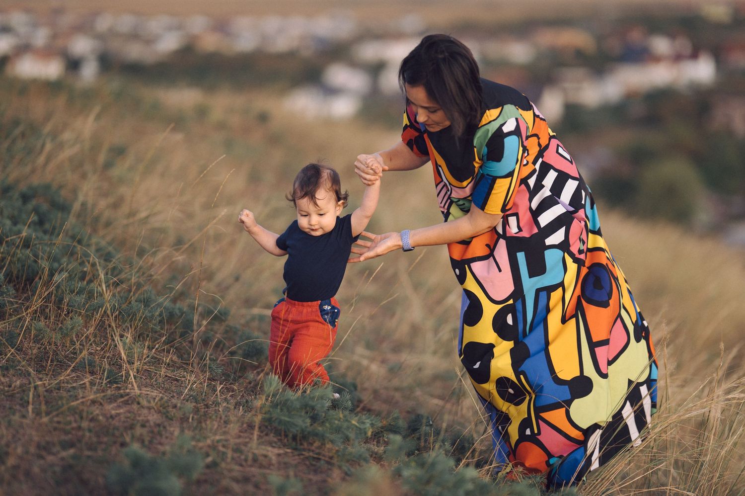 Family members in colorful outfits laugh and play together in a grassy outdoor setting at sunset.