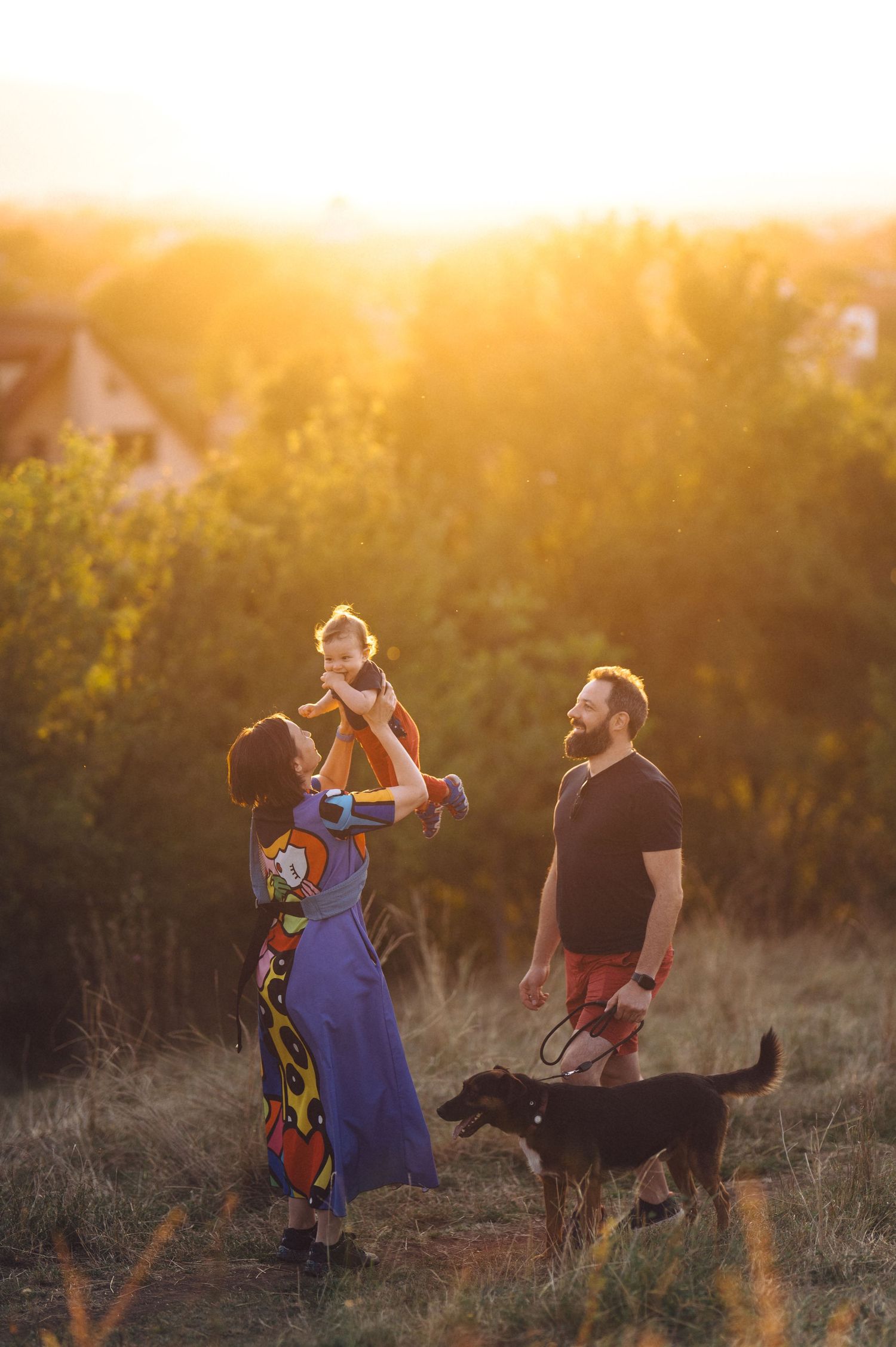 A family with a black dog enjoys a golden sunset moment in a field together during magic hour.