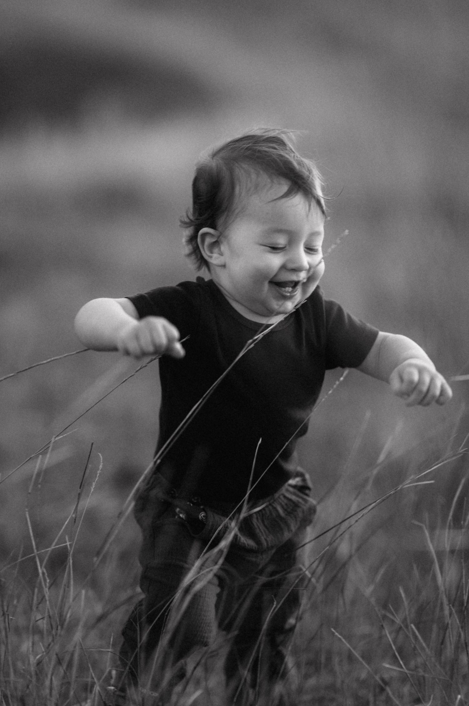 A joyful child runs and plays through tall grass in a heartwarming black and white photograph.