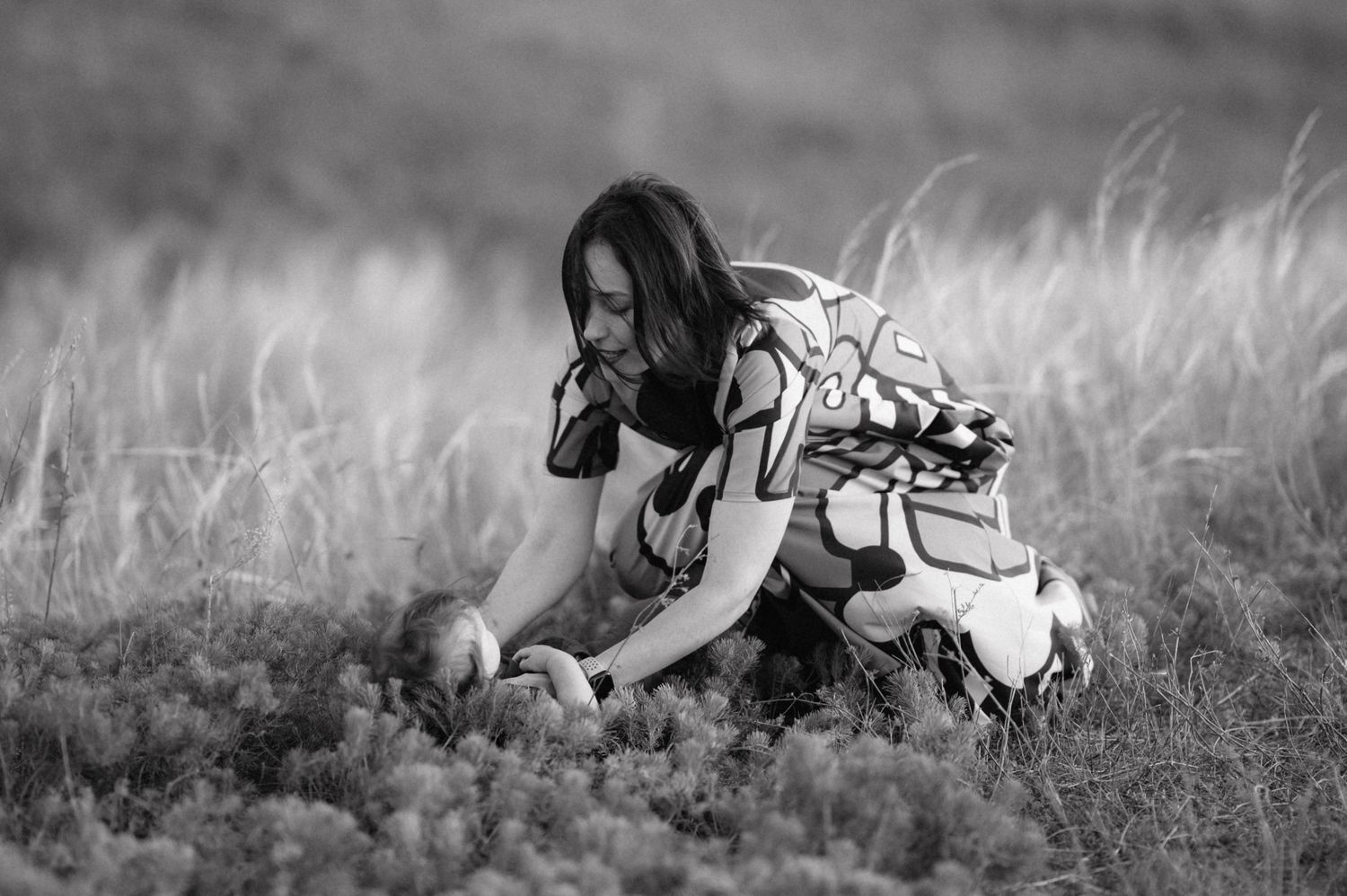 Black and white photograph of a dog playing in tall grass with a toy ball on a sunny day.