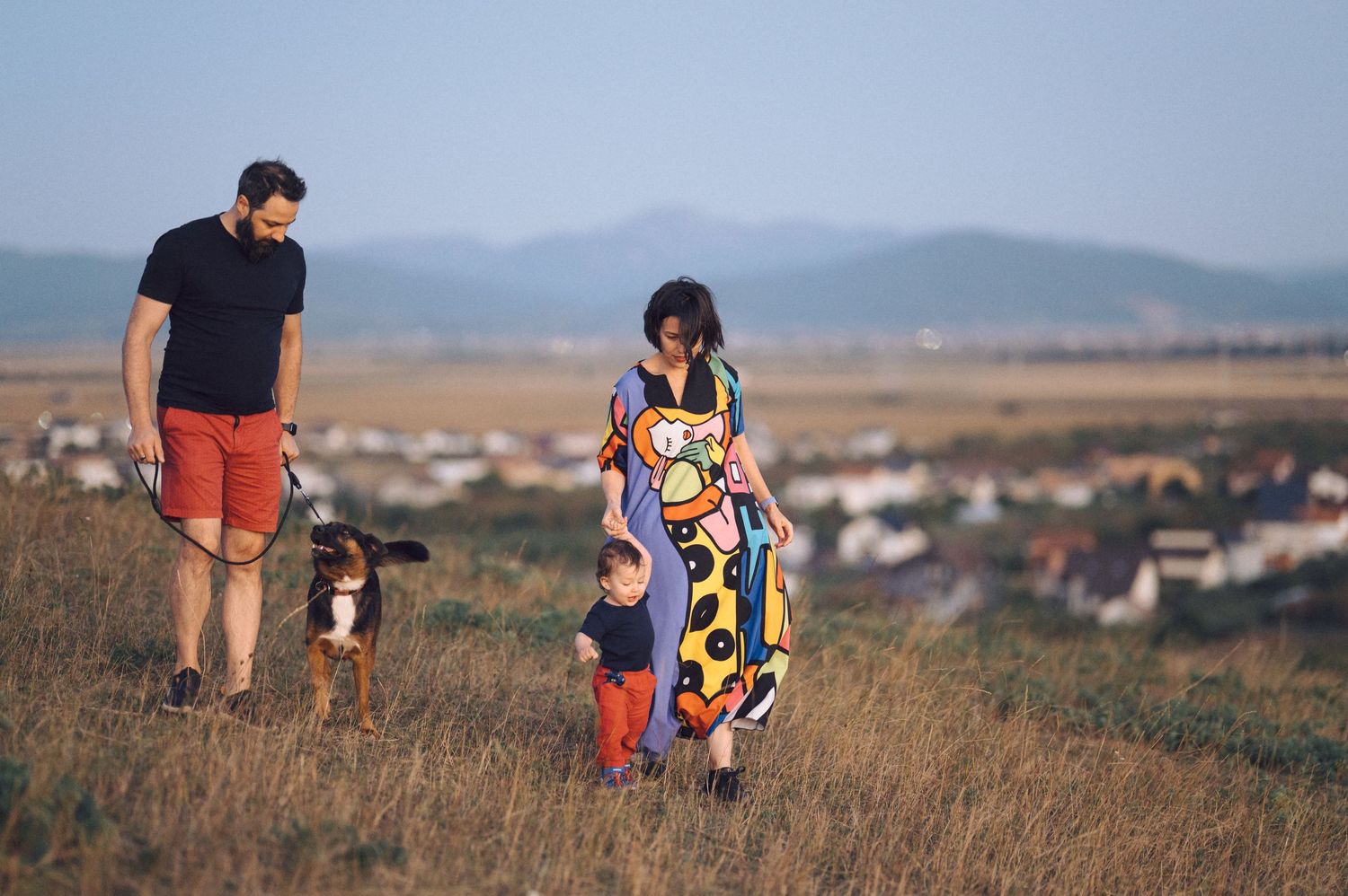 Family walking together through a grassy field with mountains visible in the background on a sunny day.