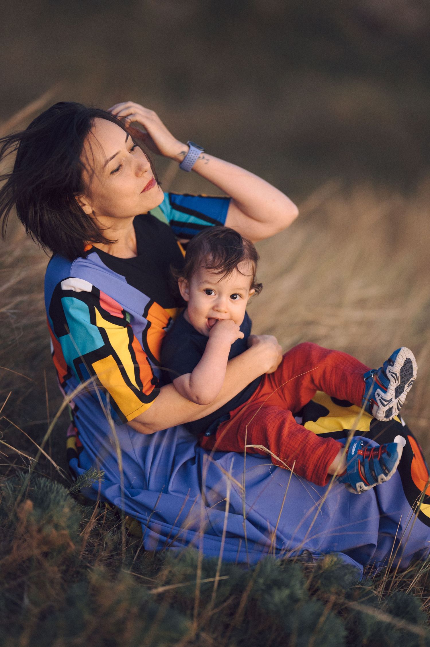 Parent and child lying in field wearing casual clothes against blurred natural background at sunset.