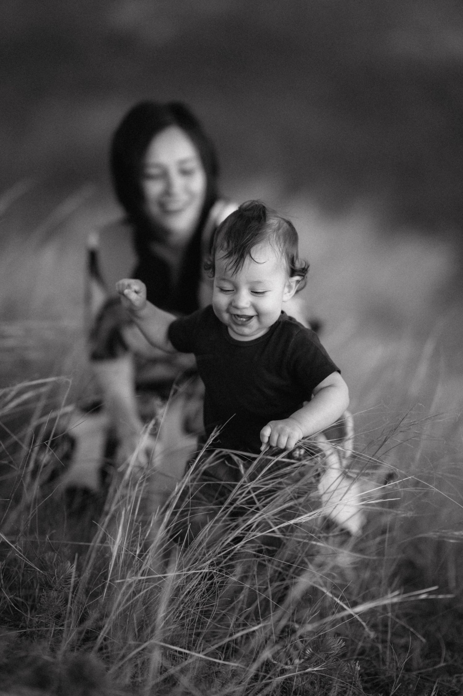 Black and white image of happy people playing in tall grass during outdoor photoshoot.