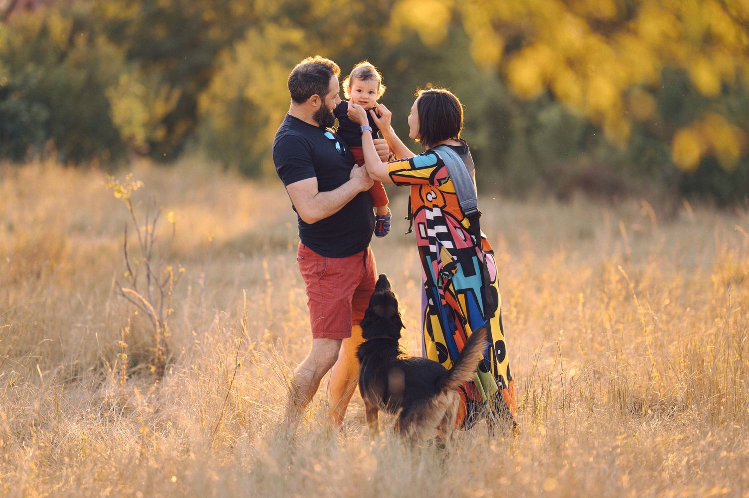 A family walks together through a golden autumn field at sunset while holding hands.