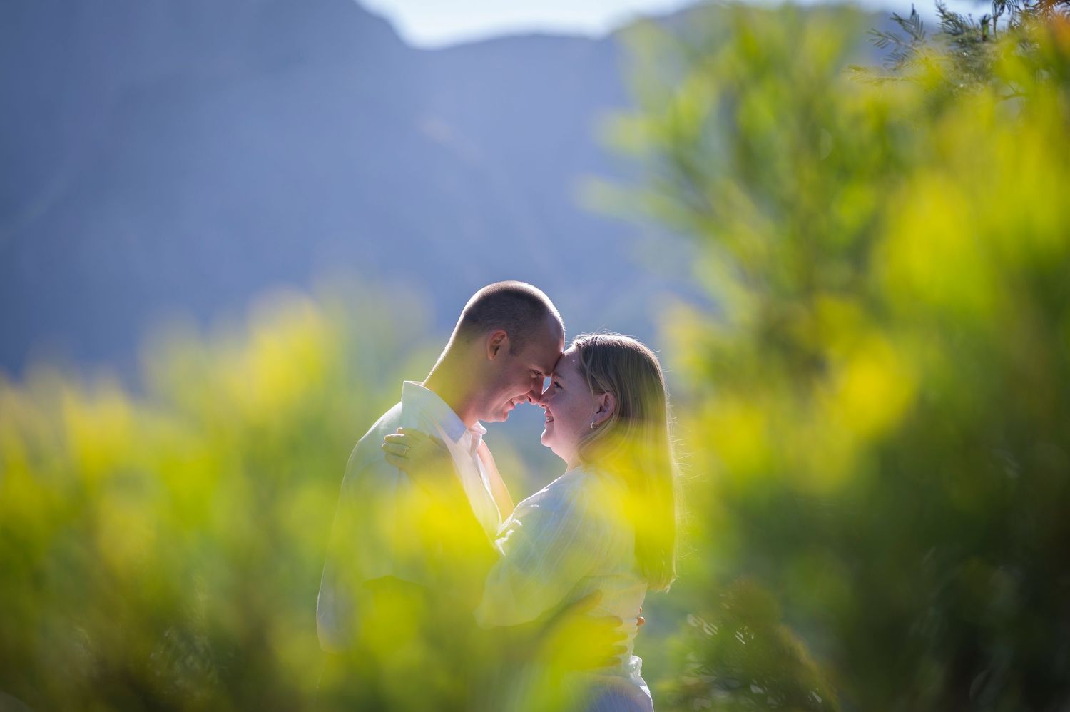 A romantic couple shares an intimate moment under a white umbrella surrounded by soft green bokeh in a summer garden.
