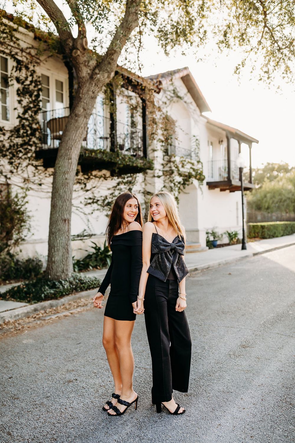 Two women laughing and walking together on a gravel path next to a white building in golden sunlight.