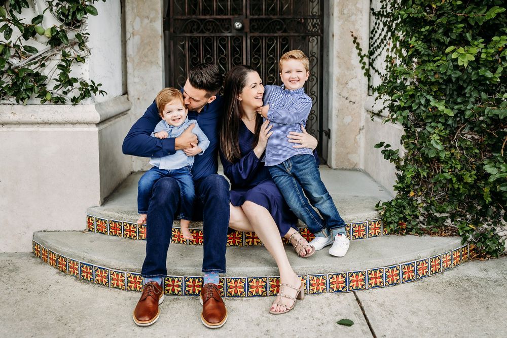 Family group sitting together on decorative tiled steps by an entrance with lush greenery.