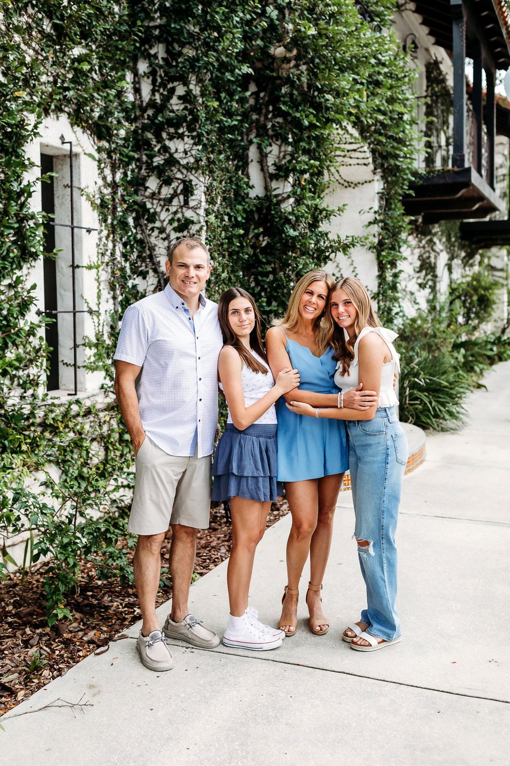 Friends posing together for casual outdoor photos near a white building surrounded by greenery.
