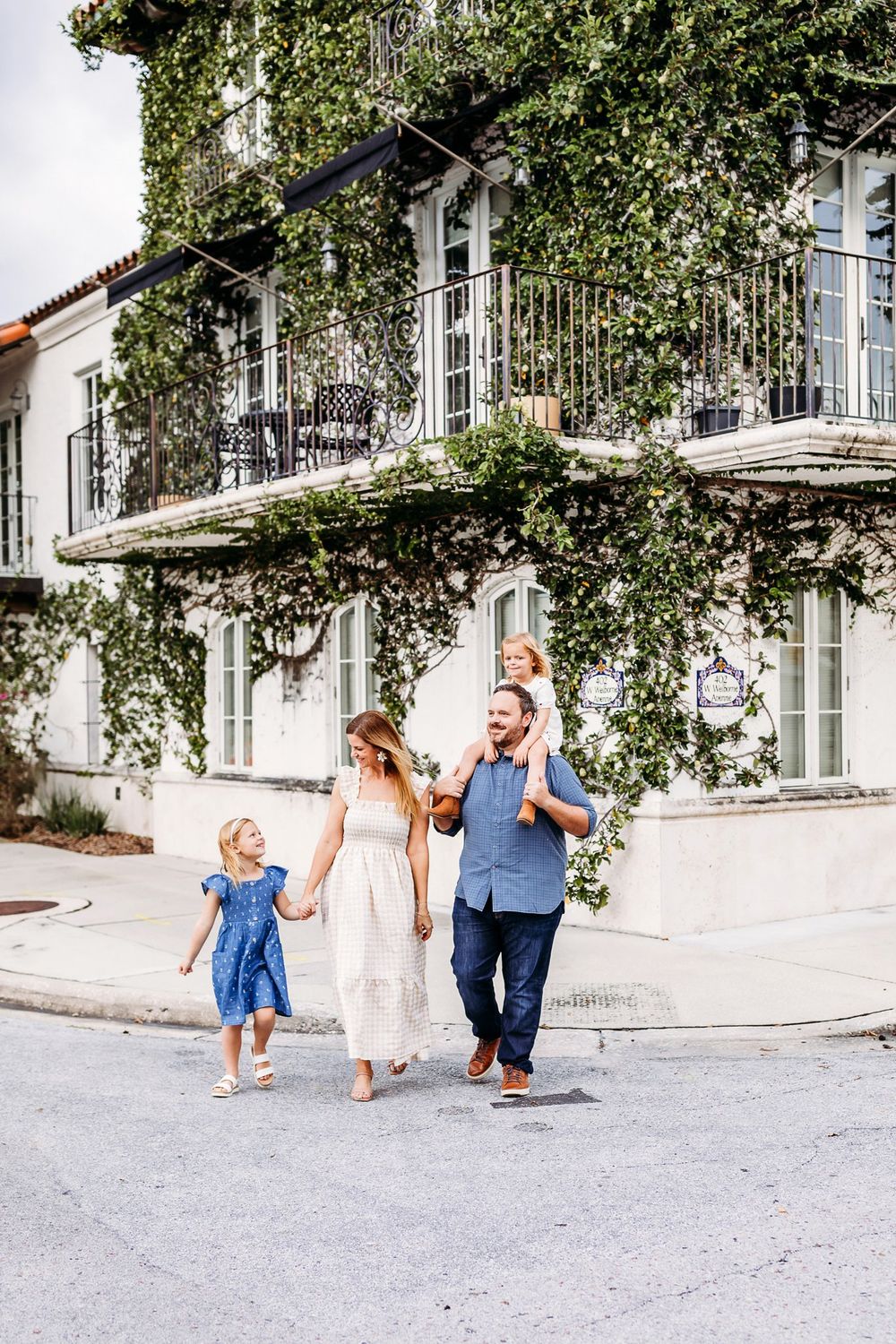 Three people walking together on a bright sunny day along white stucco buildings with trees overhead.